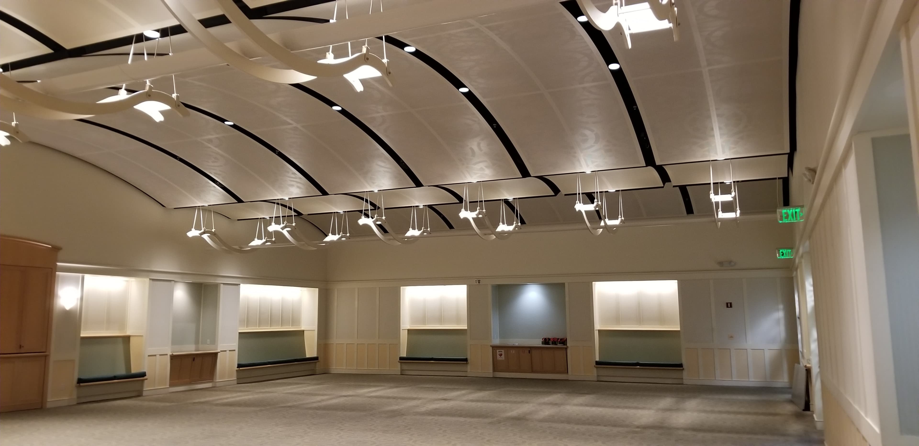 The image shows a spacious, well-lit room with a modern ceiling design and wall-mounted lighting fixtures.