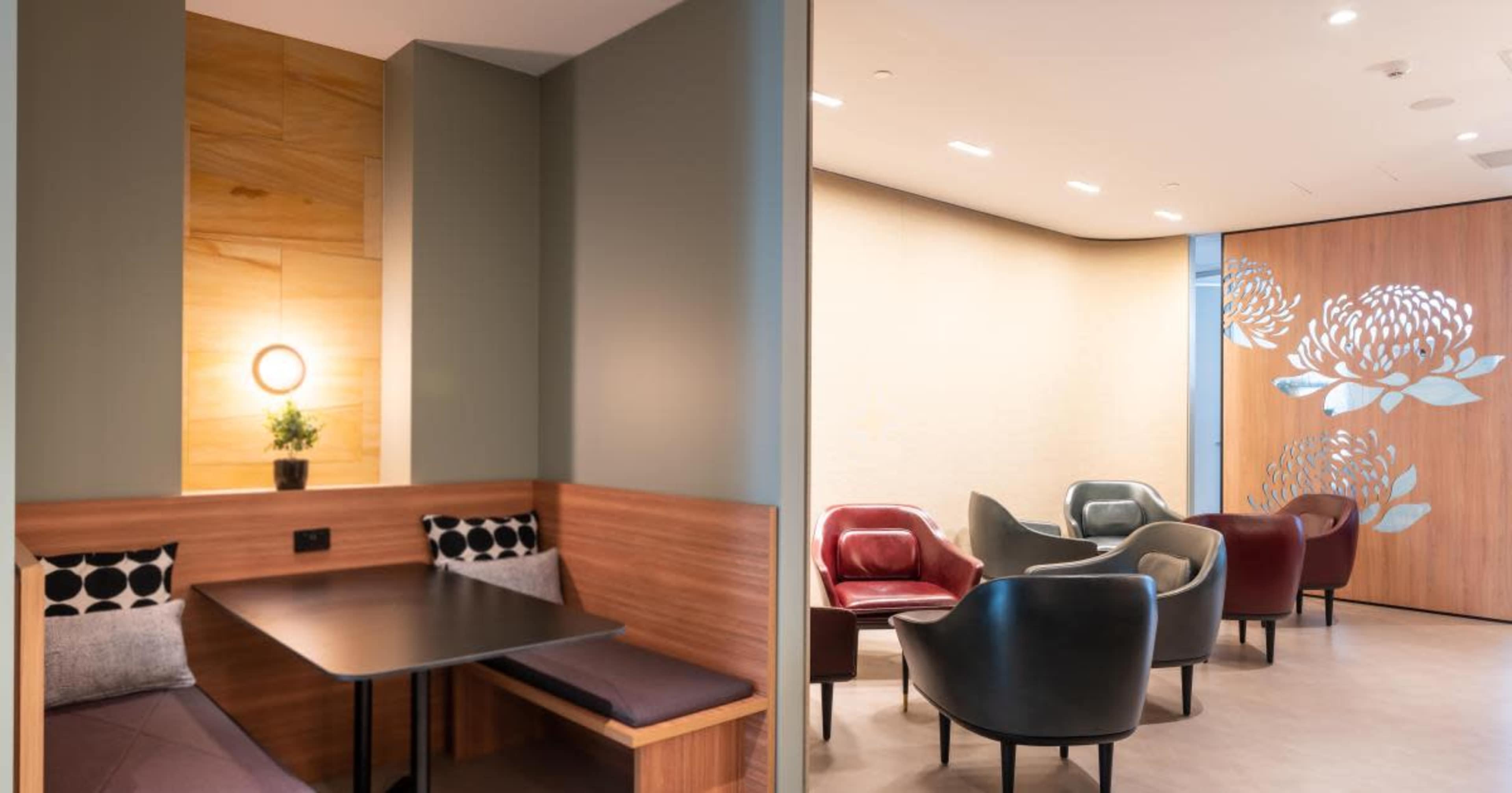 A modern lounge area featuring a cozy seating nook with a small table and a decorative wall, alongside a separate seating arrangement with contemporary chairs.