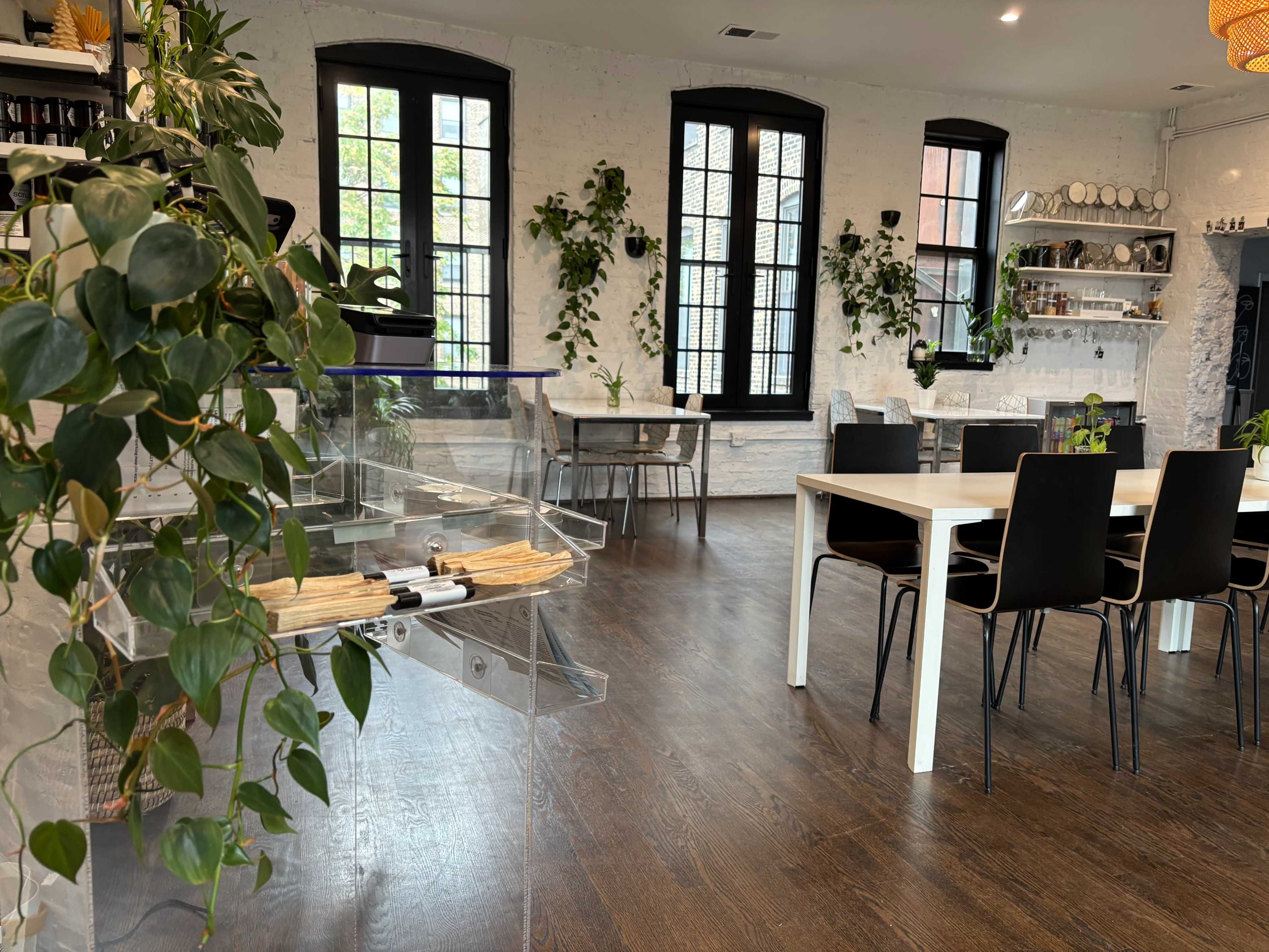 The image shows a modern dining area featuring a white table surrounded by black chairs, with a display of plants and a clear acrylic display case in the foreground.