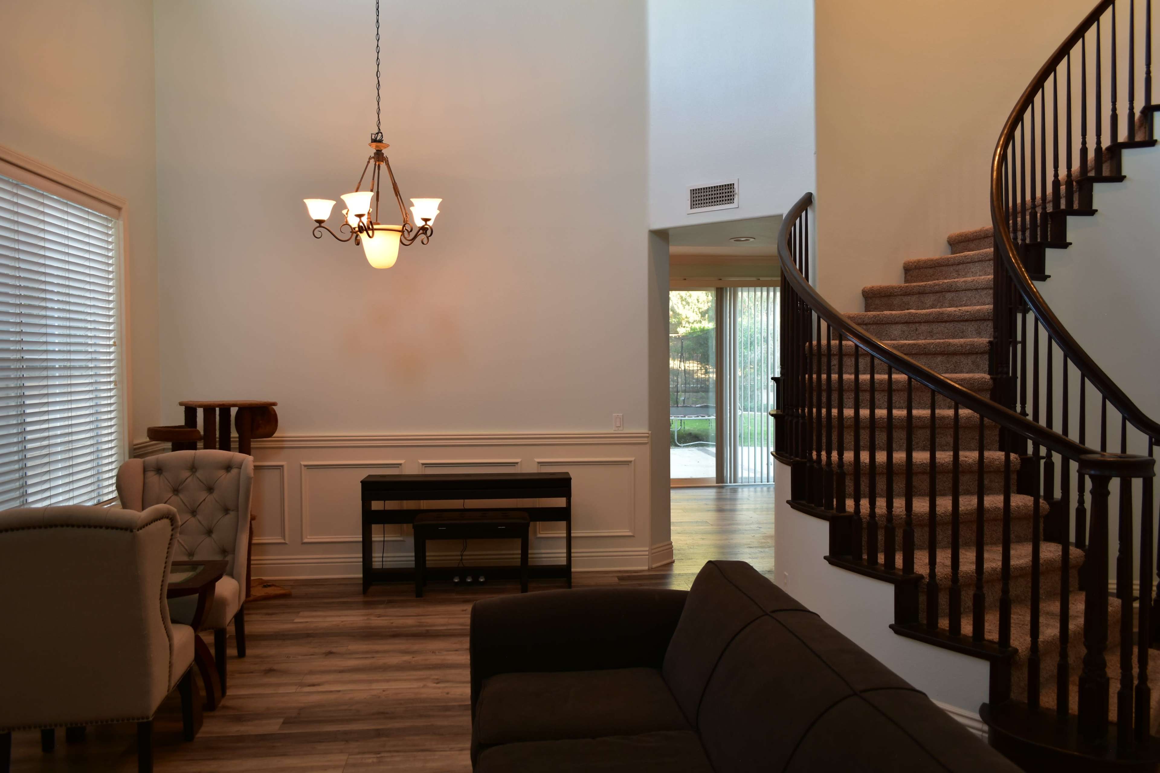 A living area with a staircase, a chandelier, and a sofa, featuring a combination of natural light and warm tones.