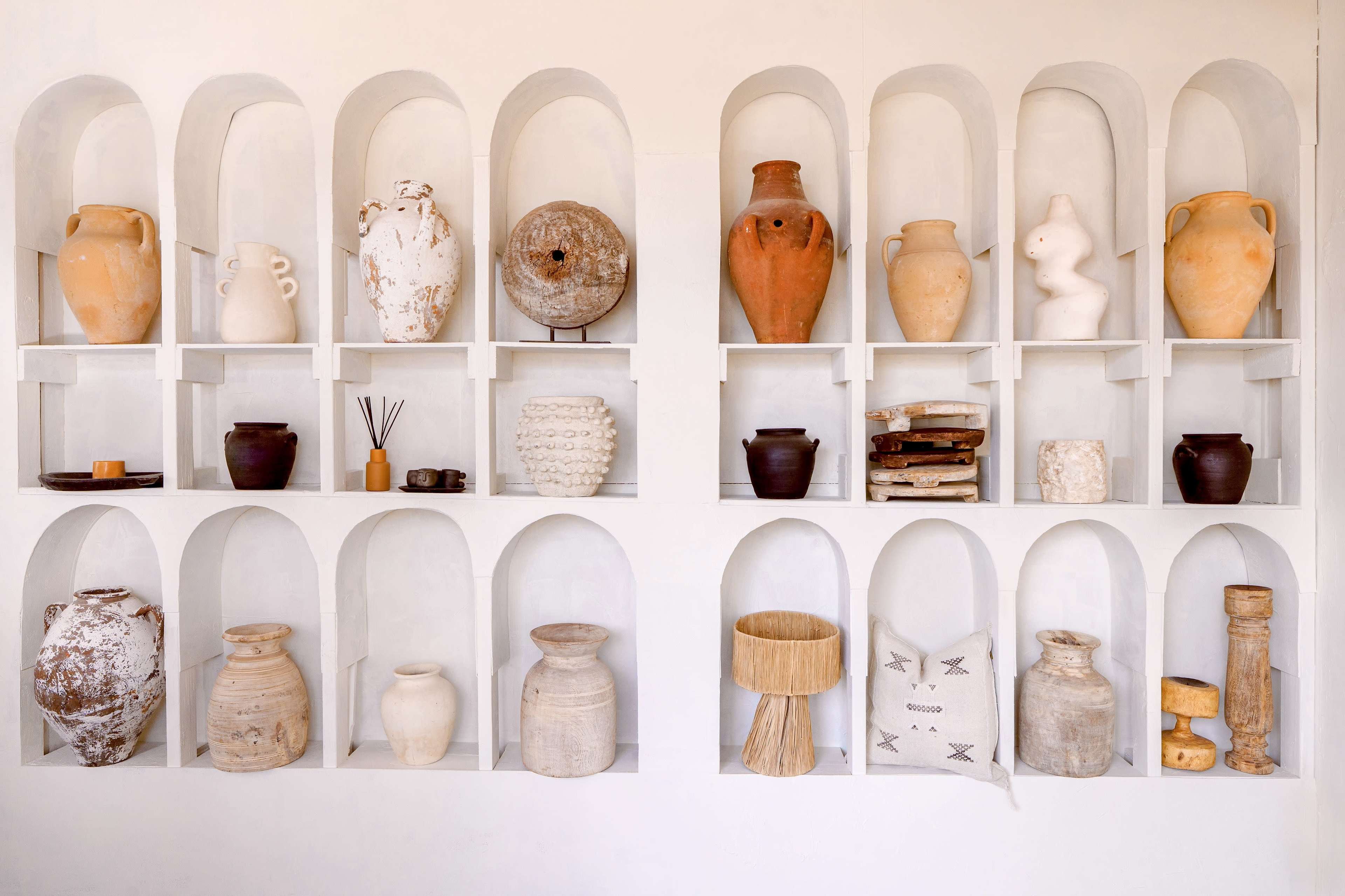 The image features a wall shelf with various ceramic and decorative artifacts organized in arched niches.