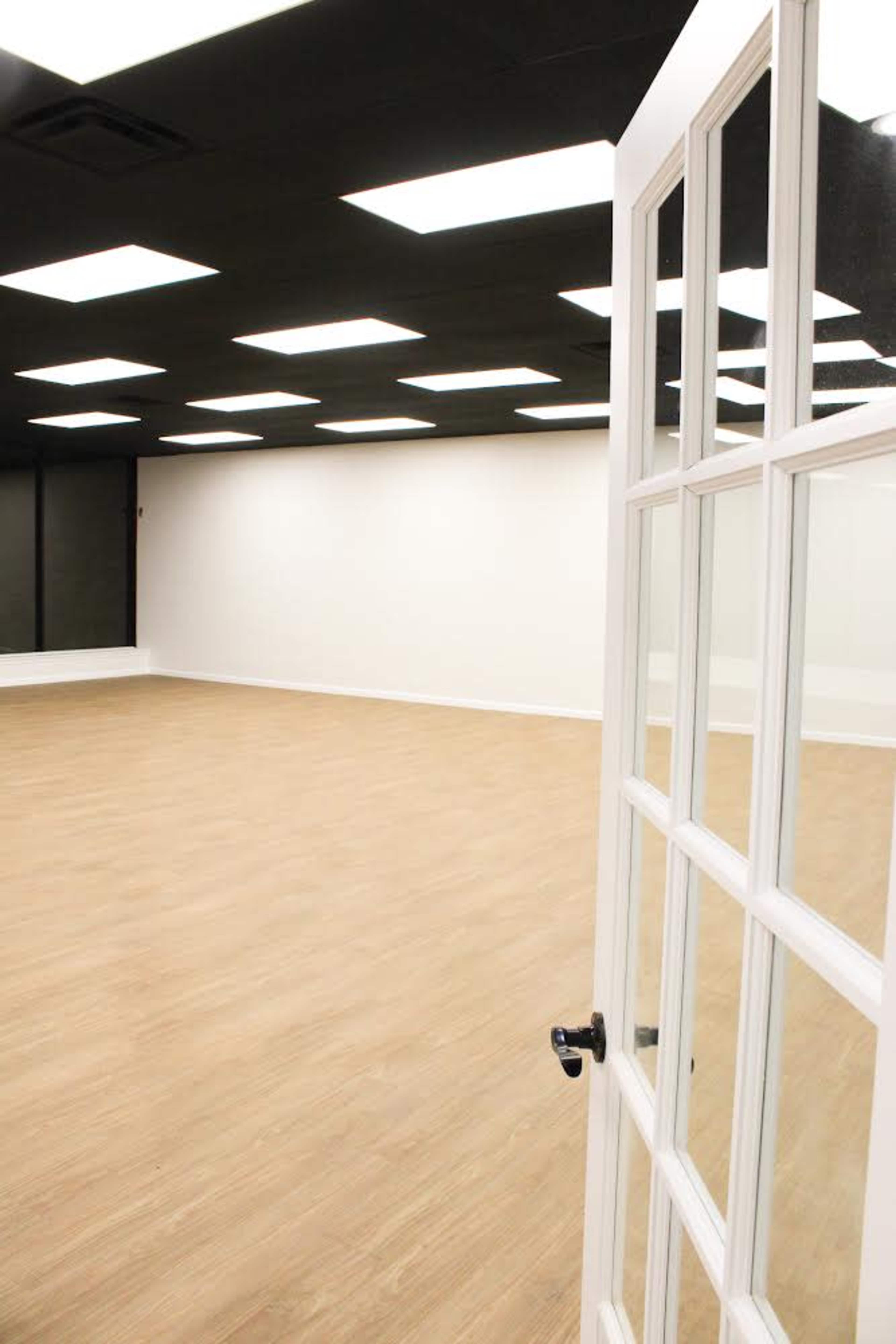 A view of an empty room with wooden flooring and a partially open glass-paneled door leading into the space.