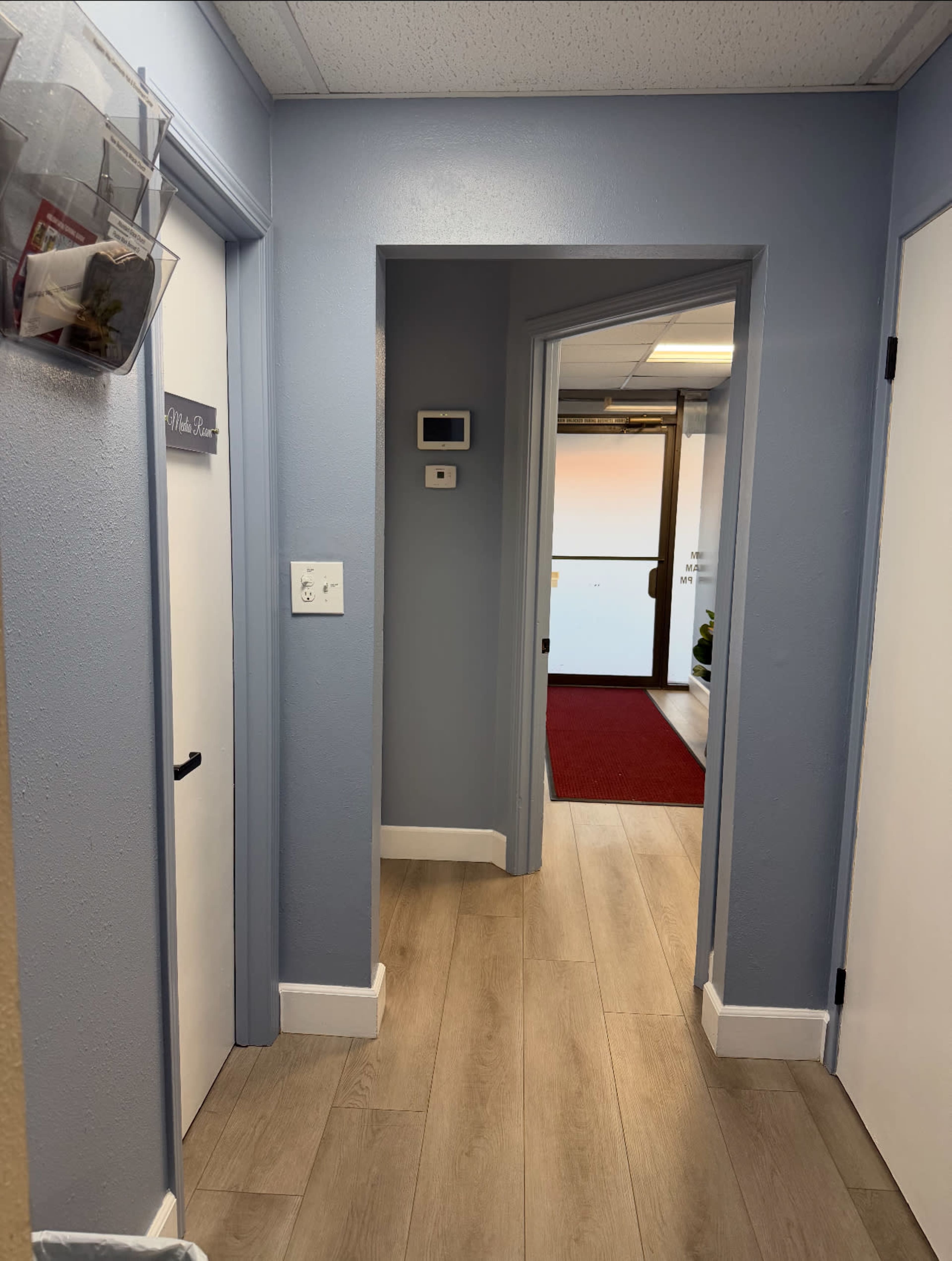 The image shows a narrow hallway with blue walls, light wood flooring, and doors on either side leading to different rooms.