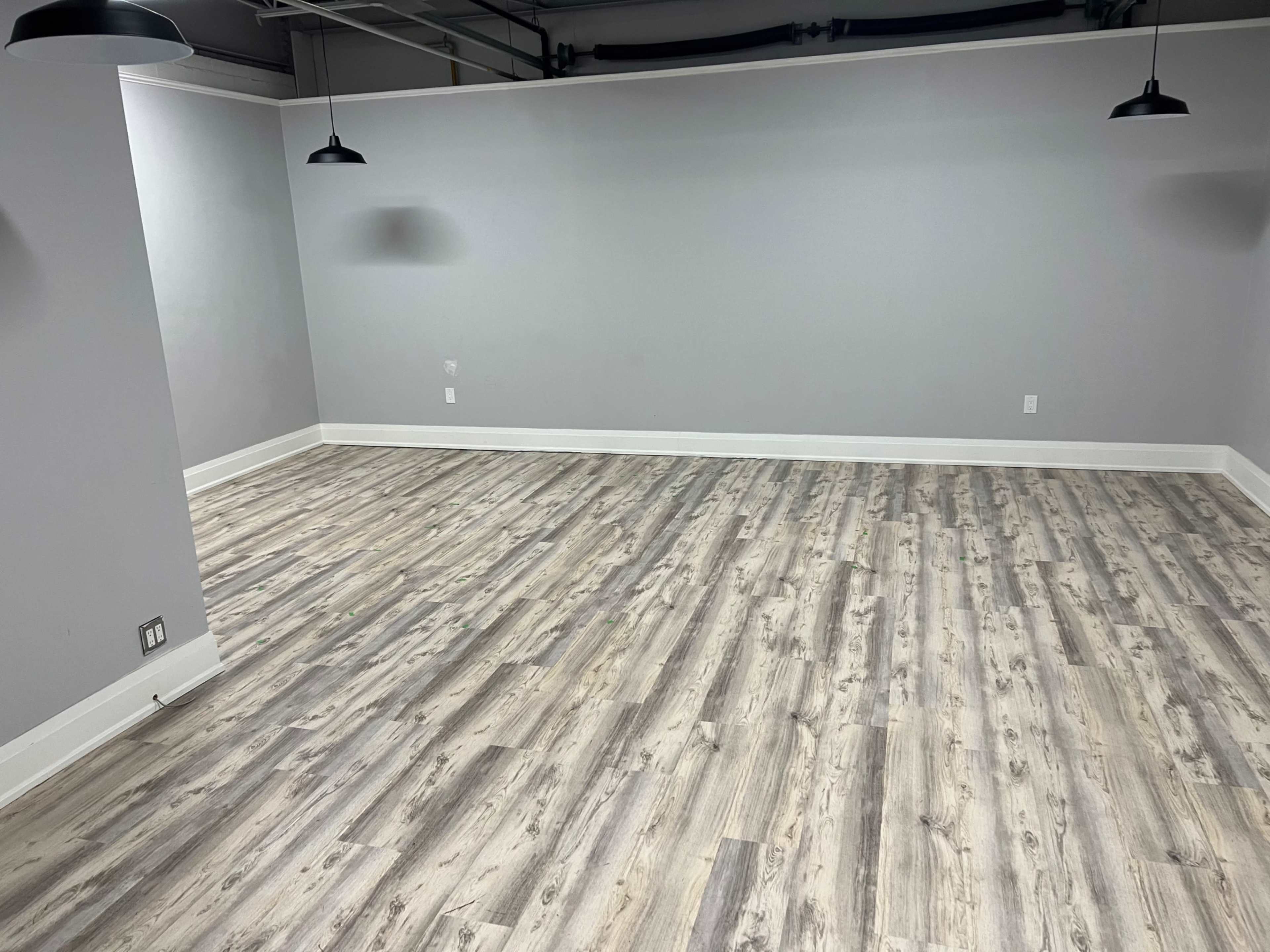 A vacant room with gray walls, a wooden floor, and two pendant lights hanging from the ceiling.