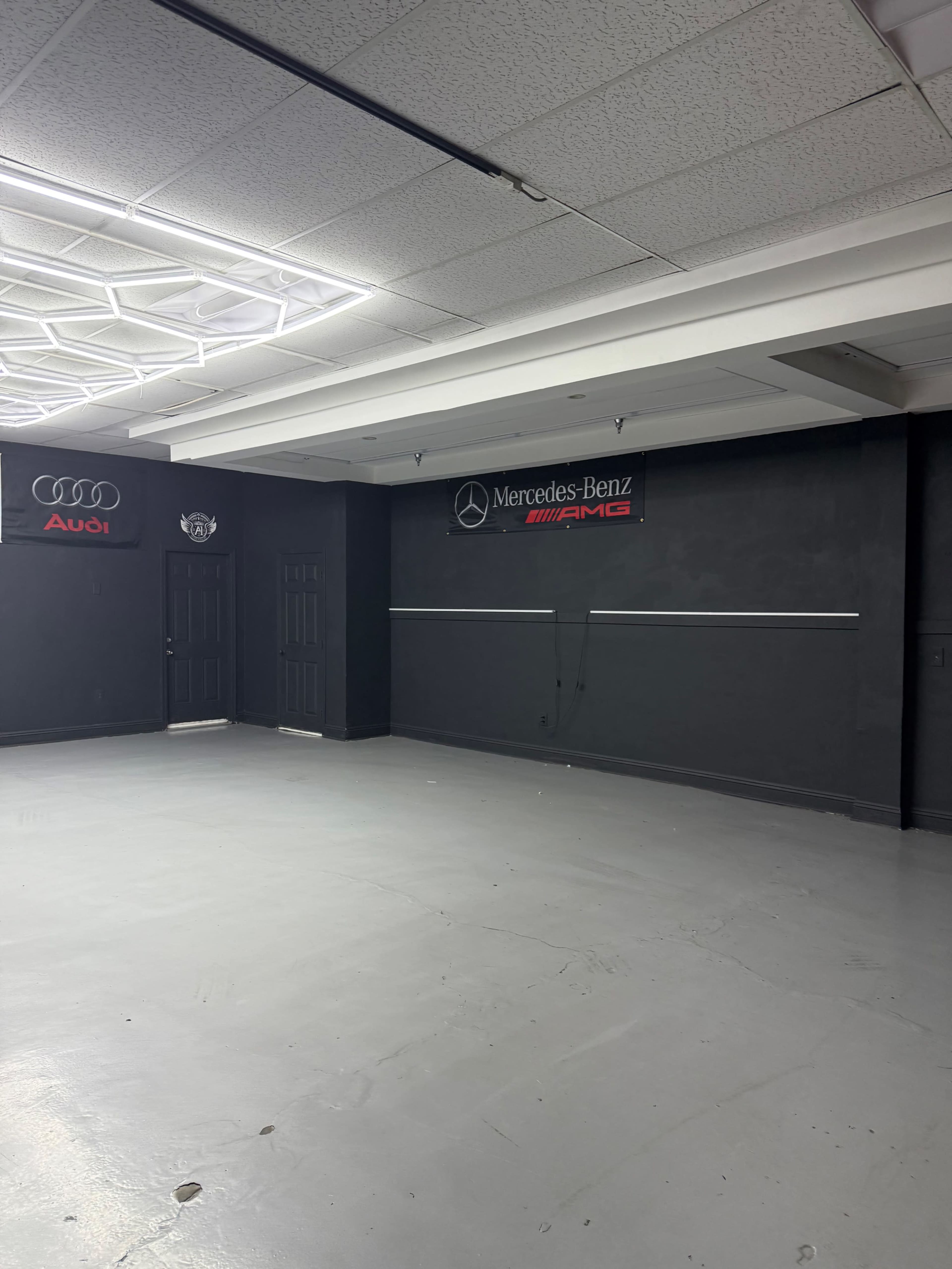 The image shows a spacious, empty garage with black walls and logos for Audi and Mercedes-Benz displayed on the wall.