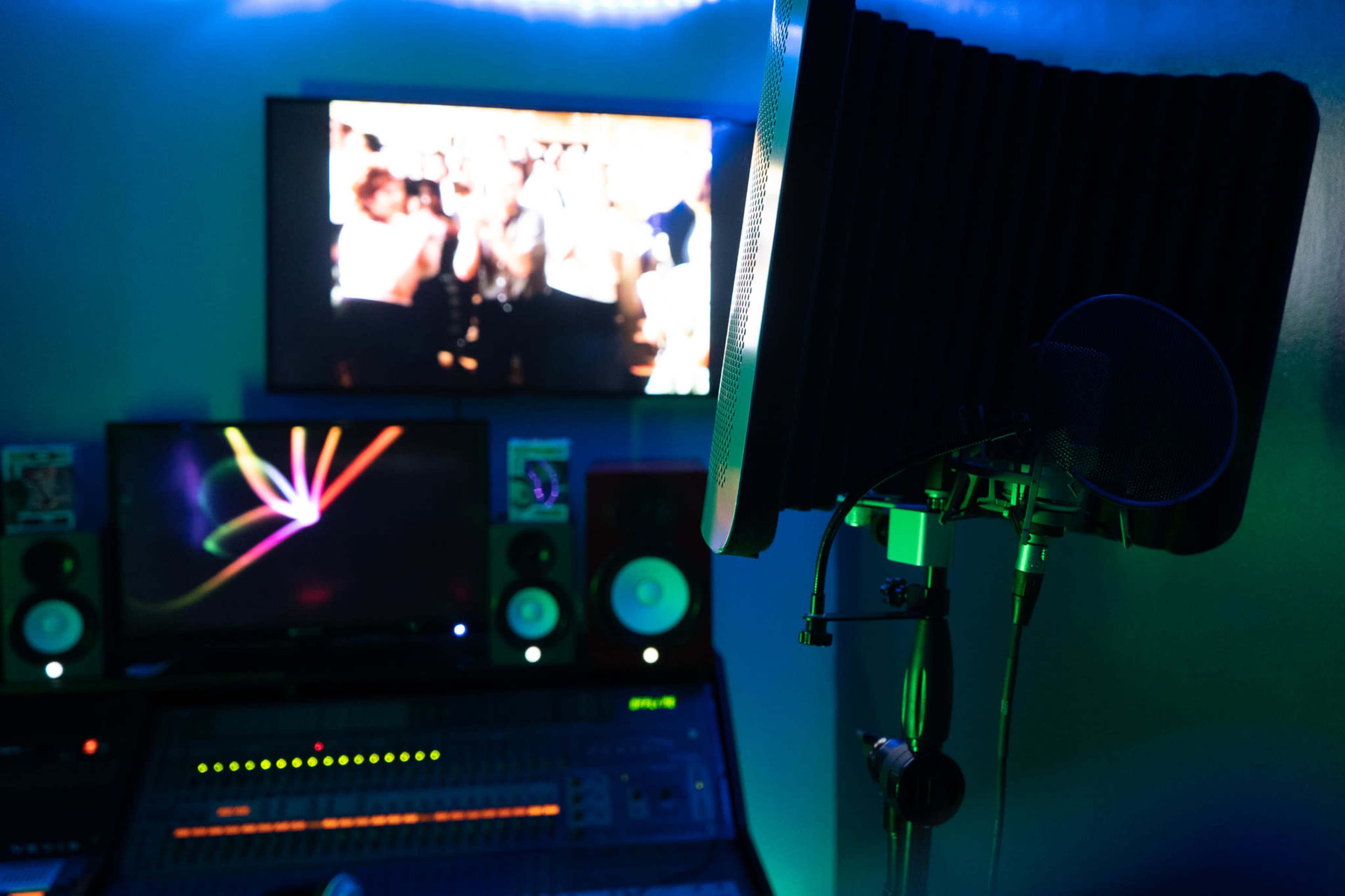 A recording studio is shown, featuring a microphone and pop filter in front of multiple computer screens and speakers.