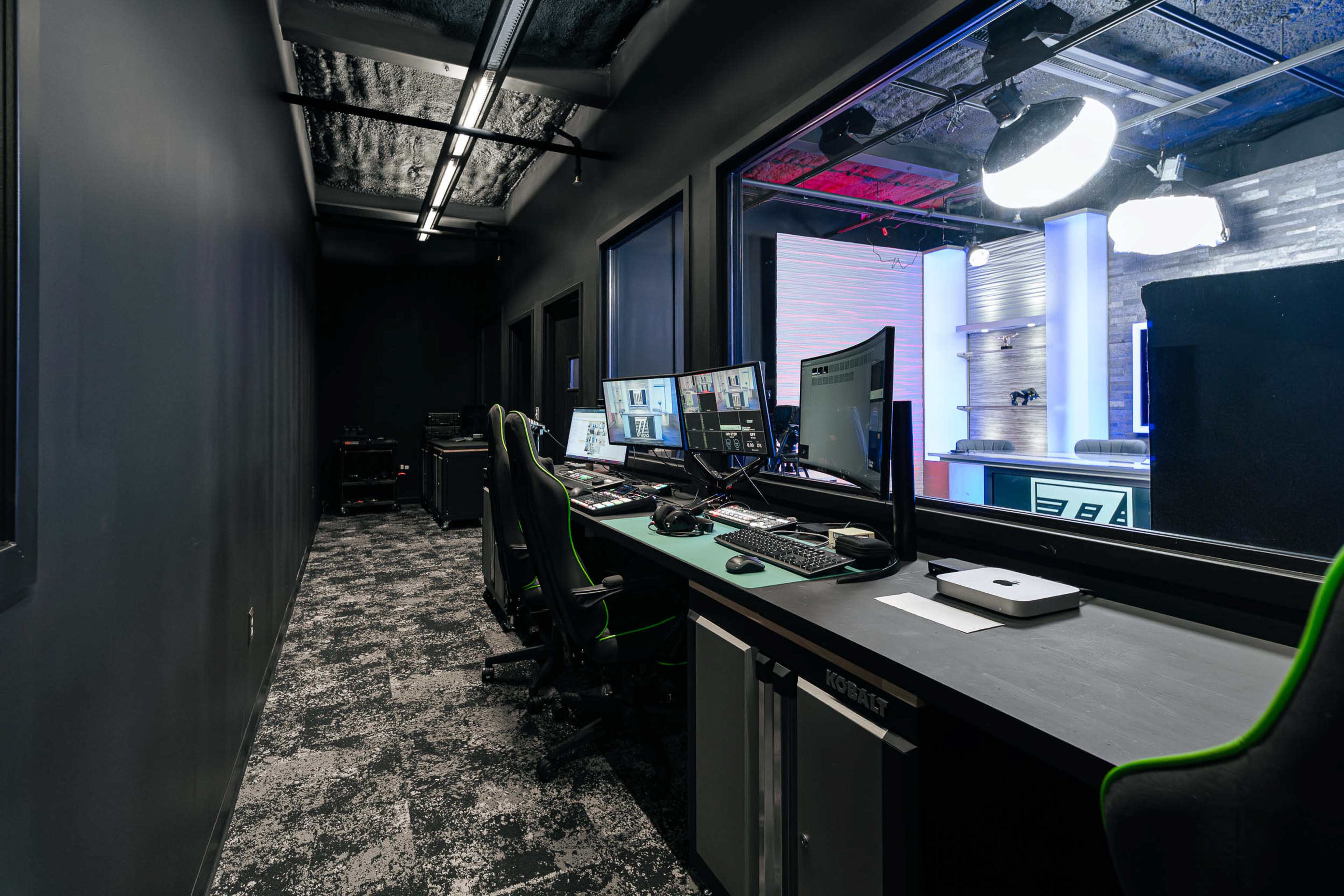 The image shows a production control room with multiple computer stations and equipment set against a dark hallway.