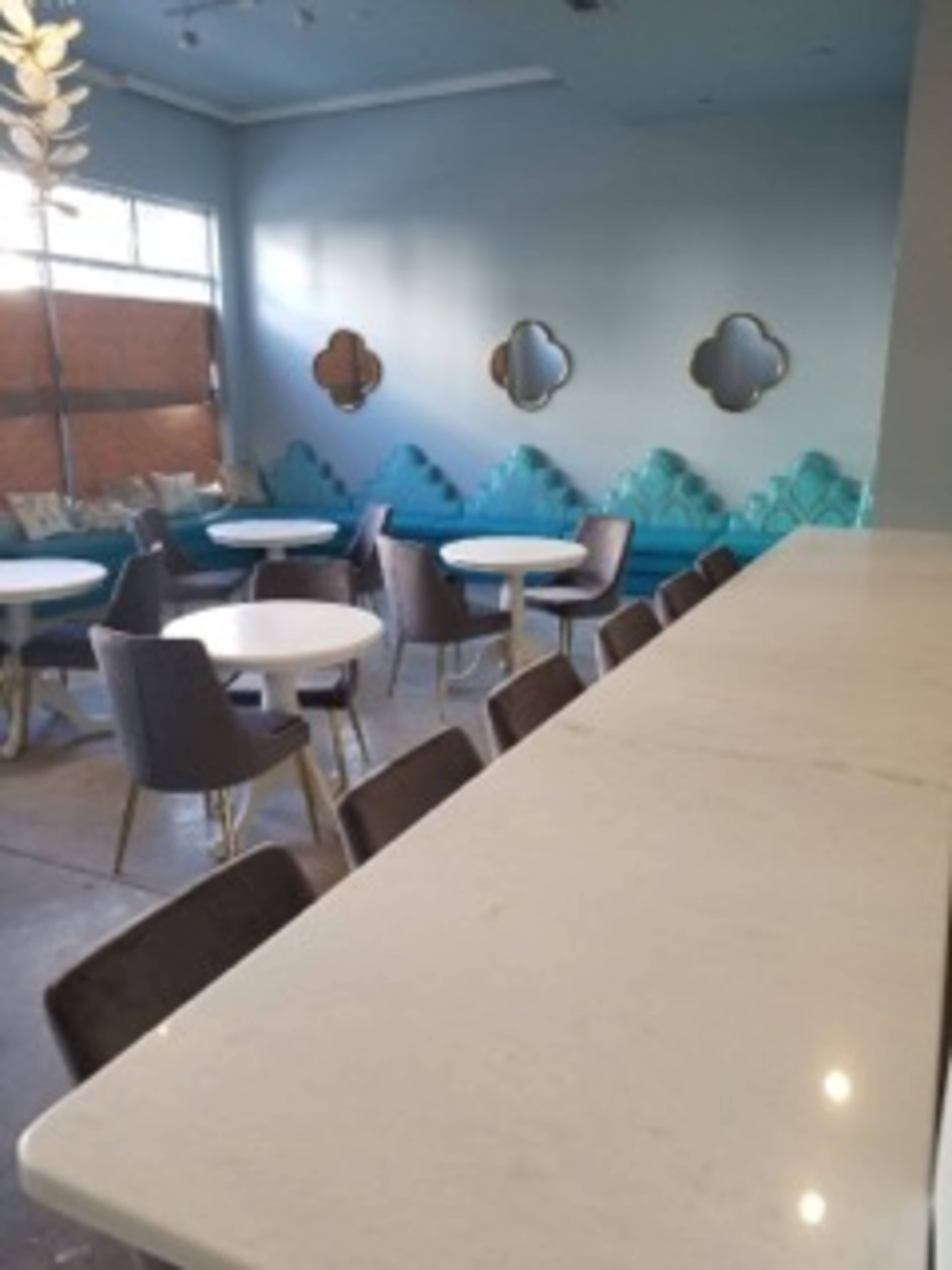 The image shows a modern café interior featuring round tables, plush seating against a blue wall, and a clean white countertop.