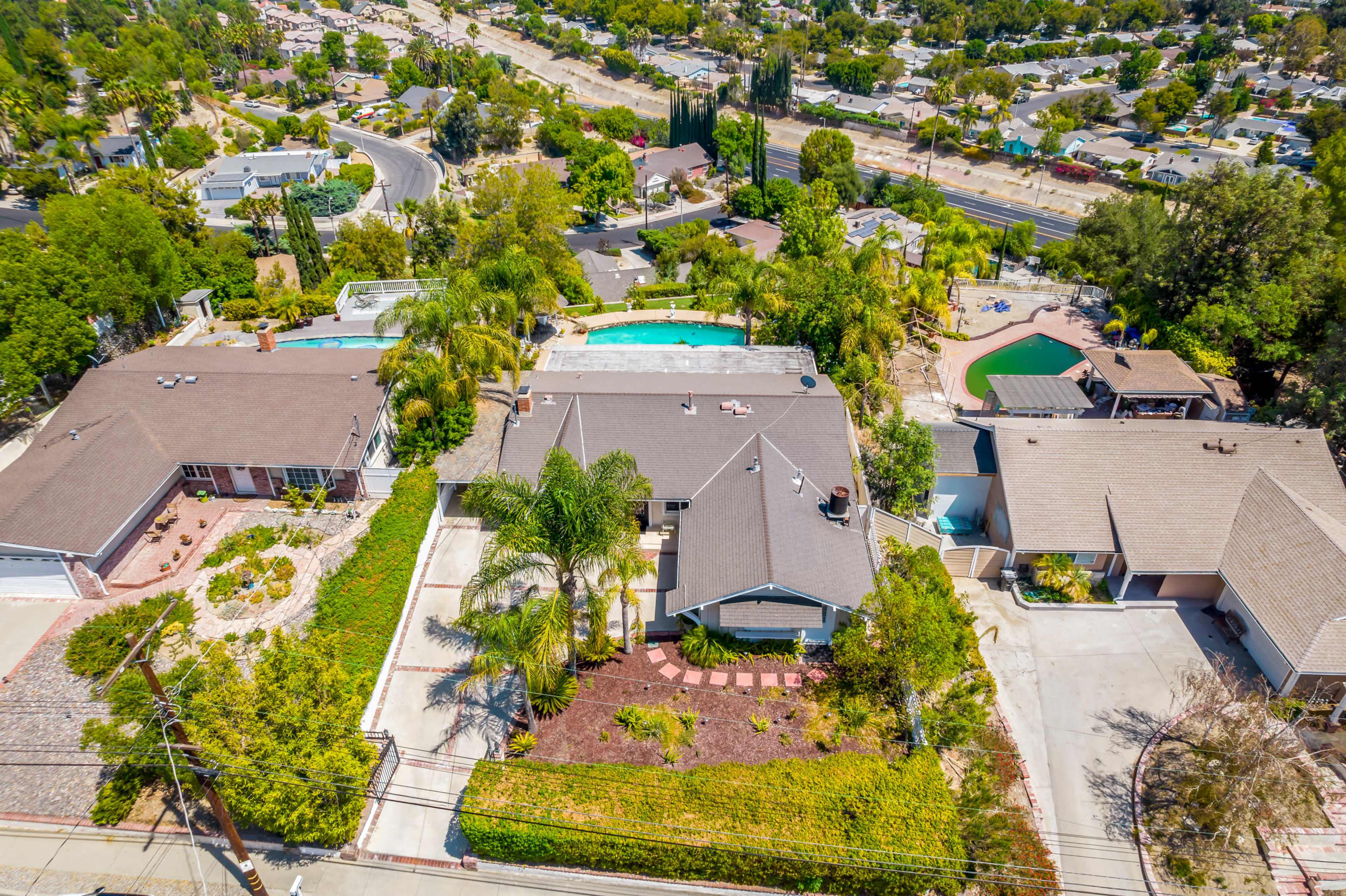 A residential area with several houses, pools, and landscaped yards set against a backdrop of greenery and roads.