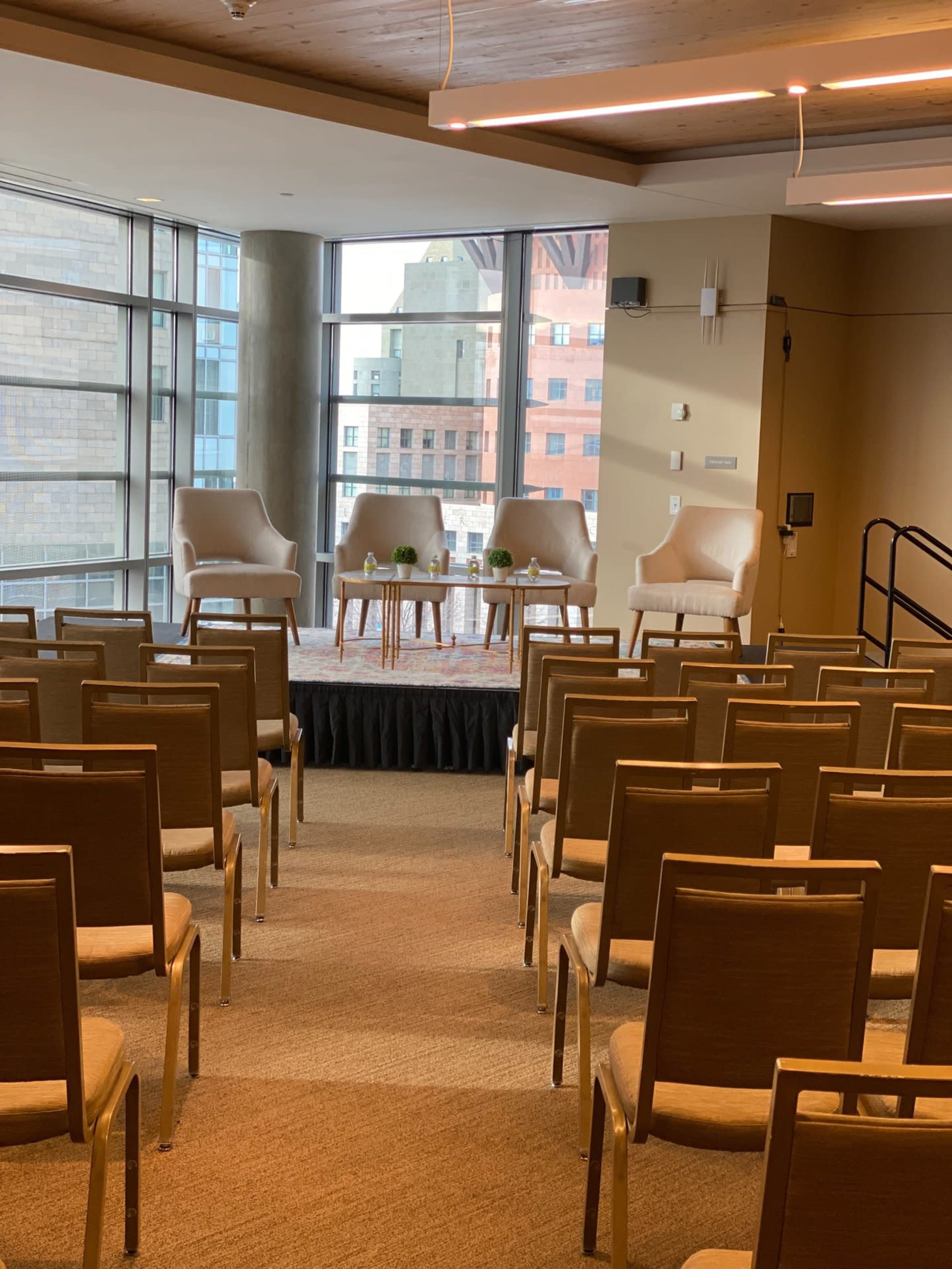 A seating area is arranged with three chairs and a small table in front of a row of empty seats facing the window.