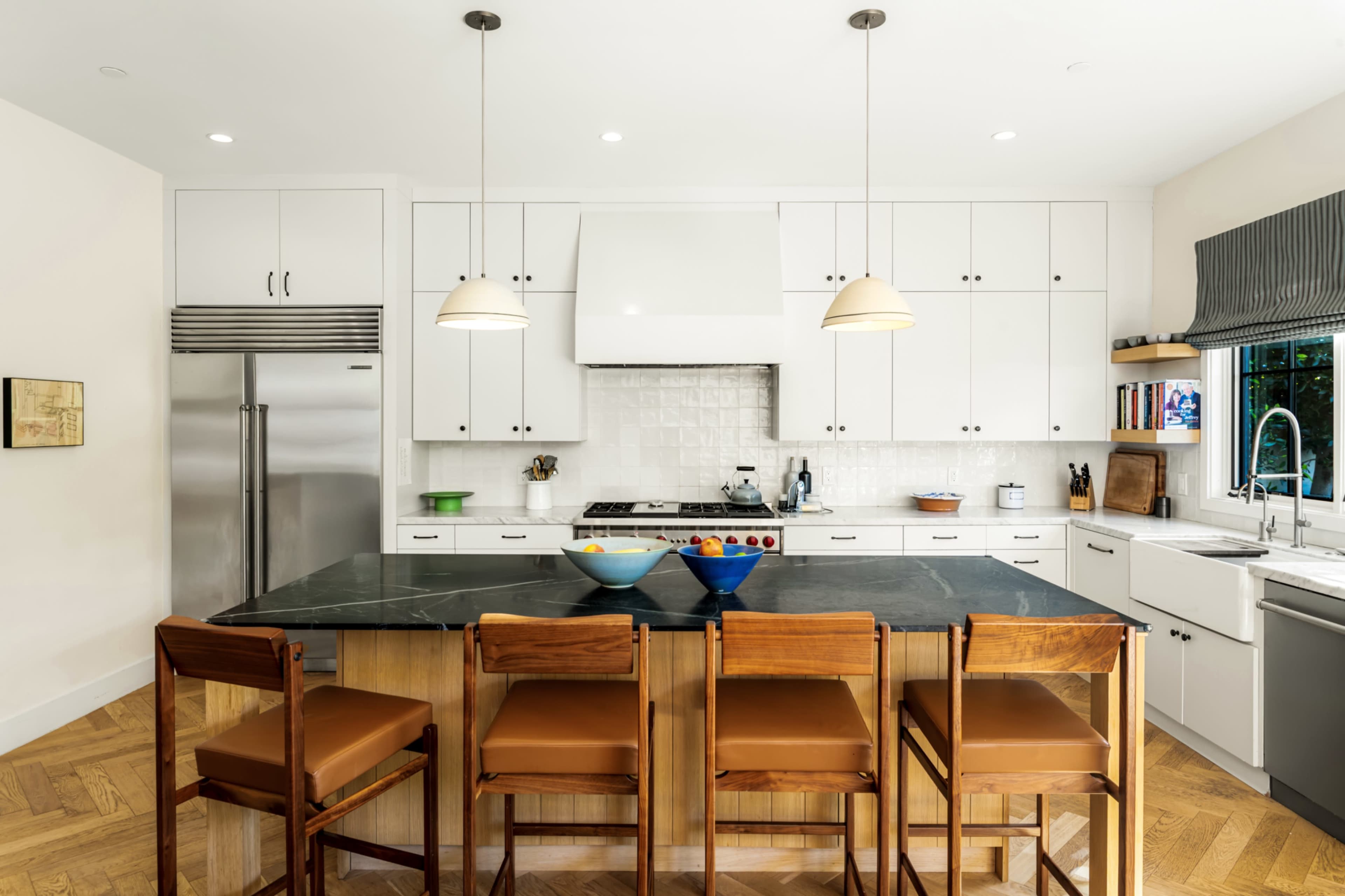 The image shows a modern kitchen with white cabinets, a large dark countertop, and four wooden bar stools arranged around the island.