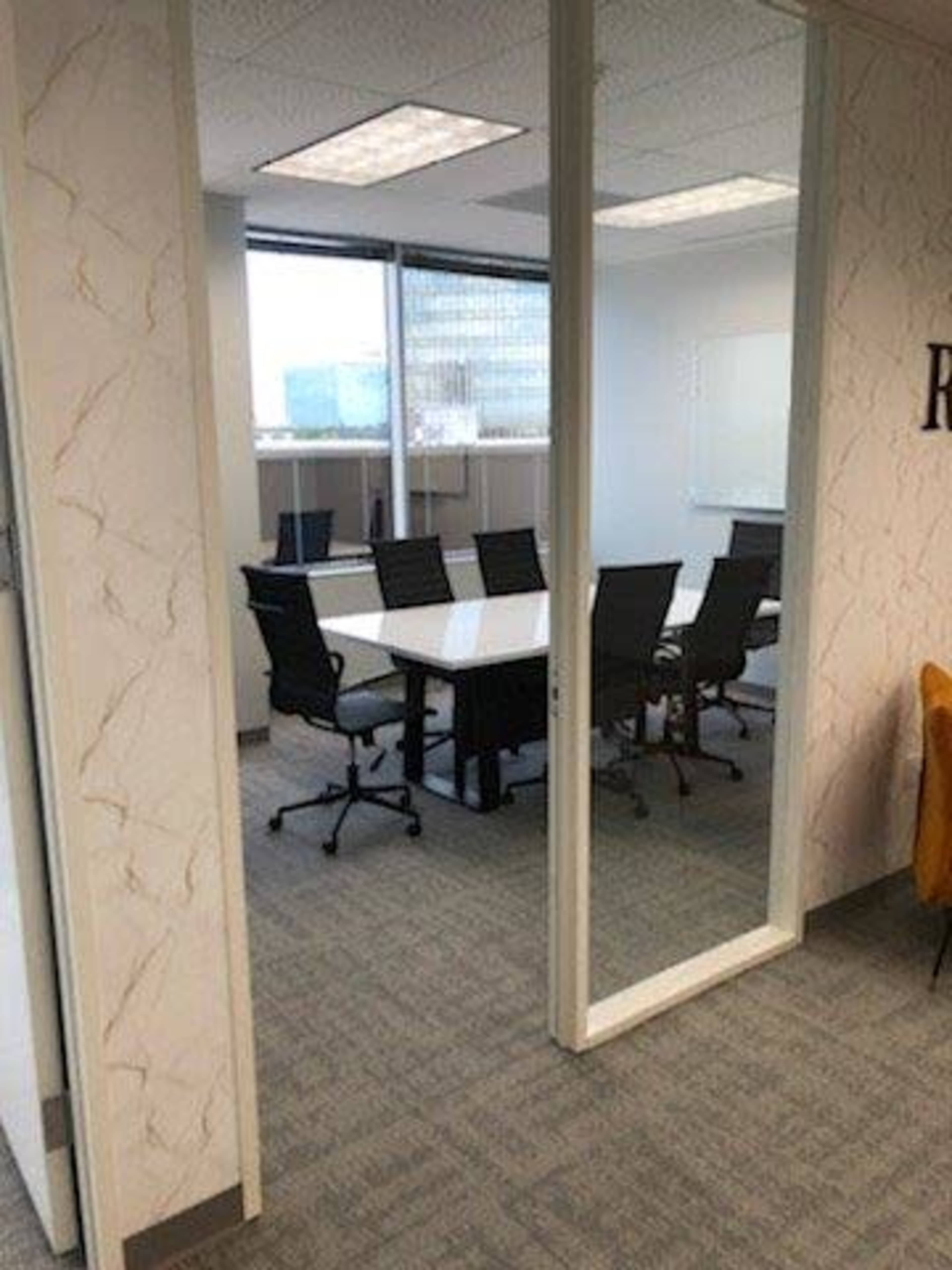 A conference room with a large table surrounded by office chairs, visible through glass walls.
