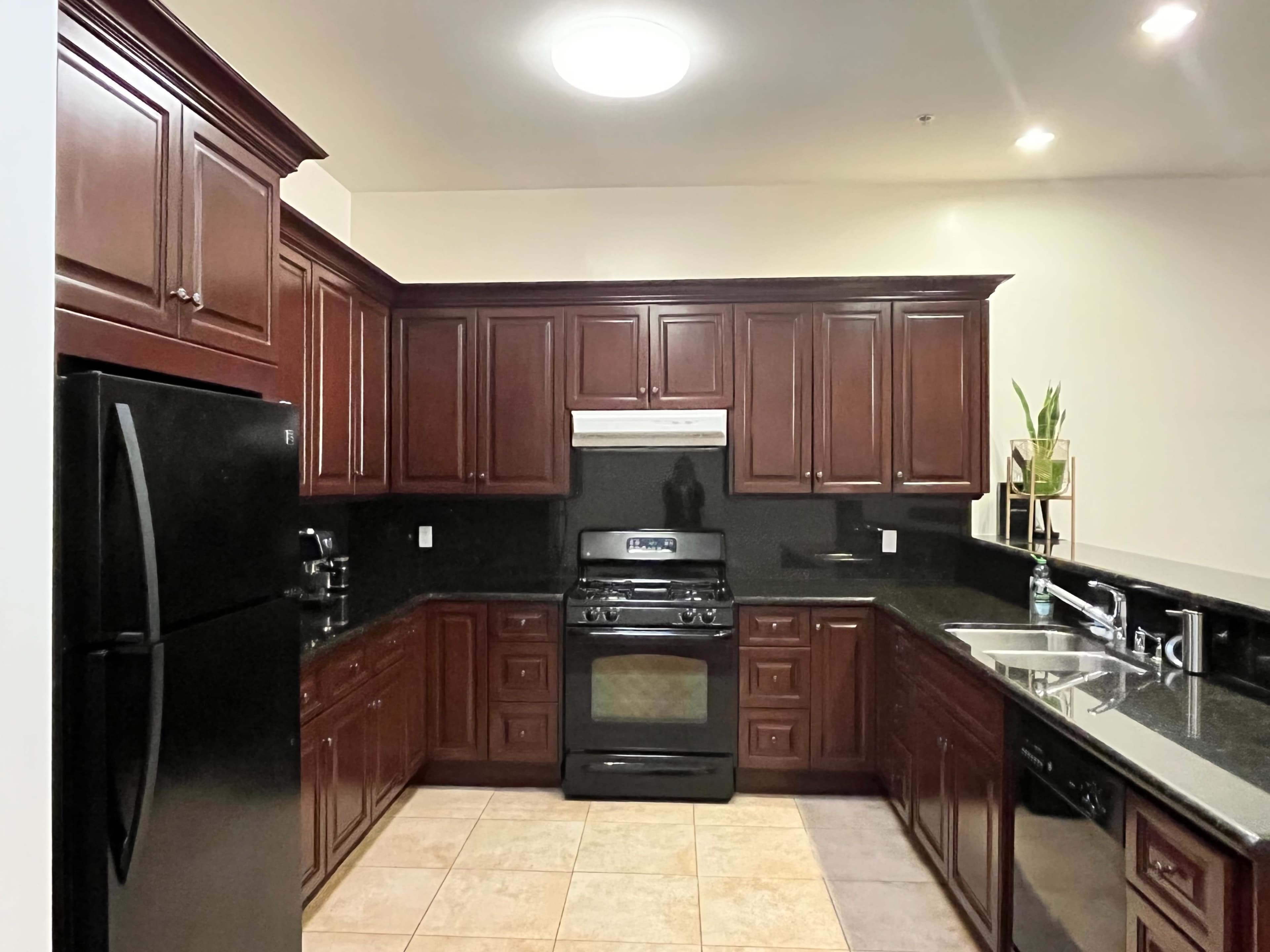 The kitchen features dark wooden cabinets, black appliances, and granite countertops with a tiled floor.
