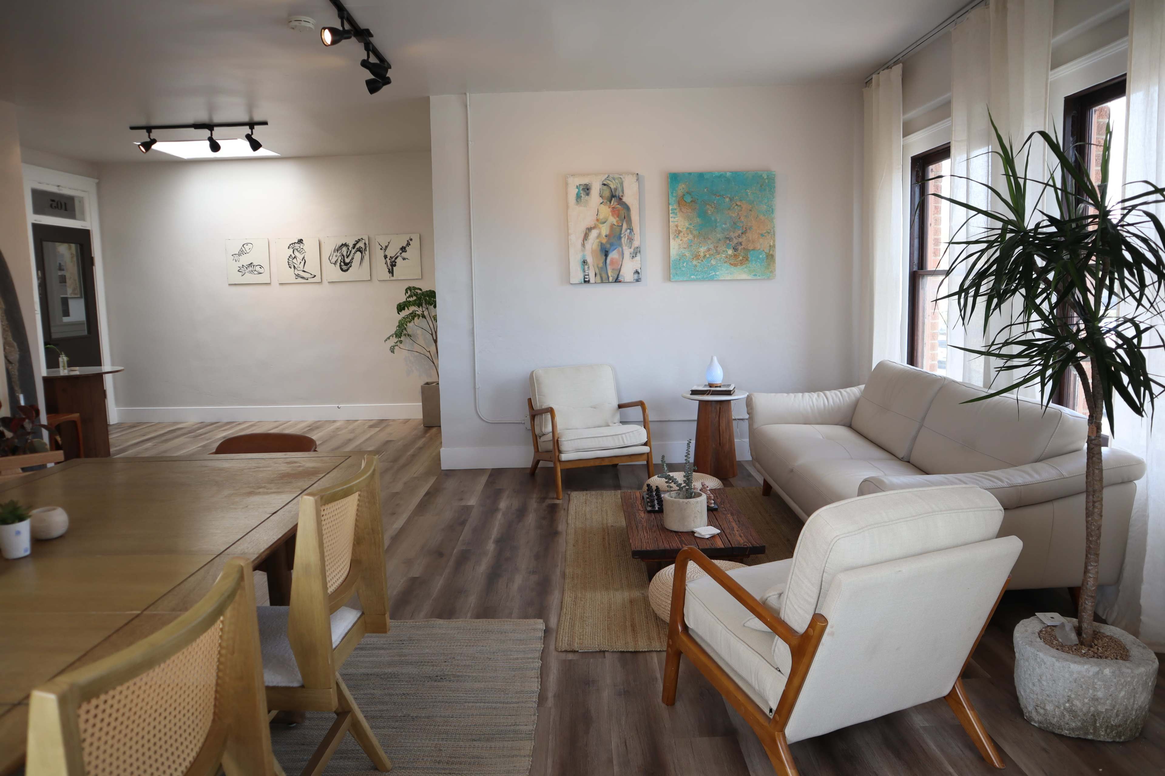 The interior features a spacious living area with a sofa, armchairs, a dining table, and artwork on the walls.
