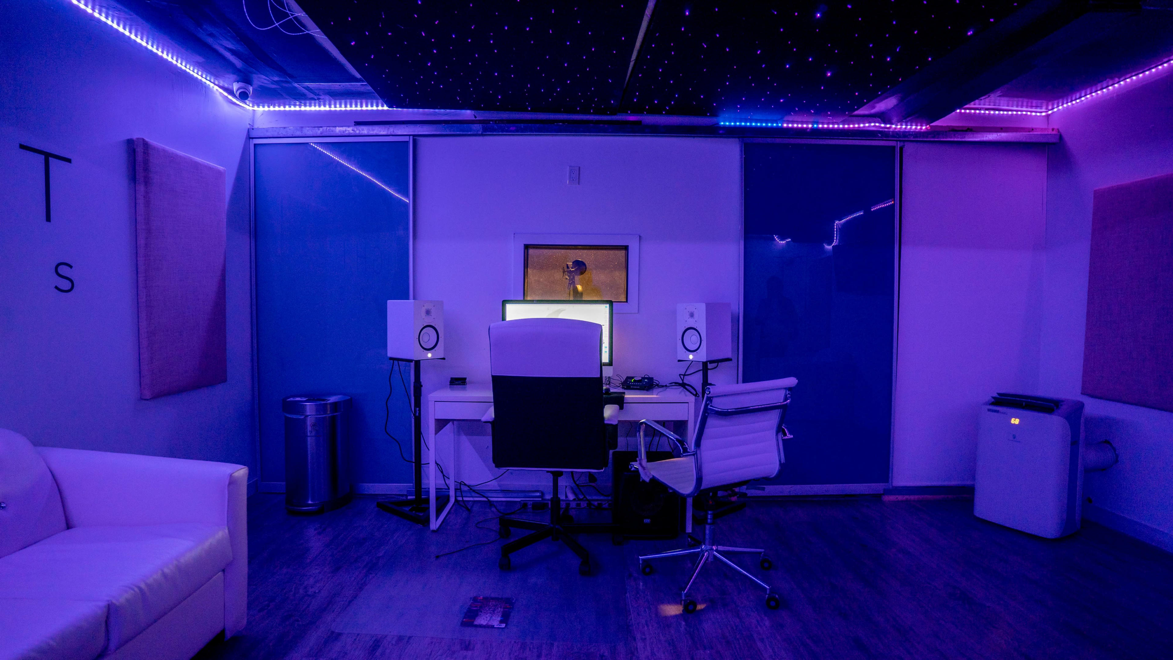 A modern recording studio with a desk, two speakers, and ambient lighting.