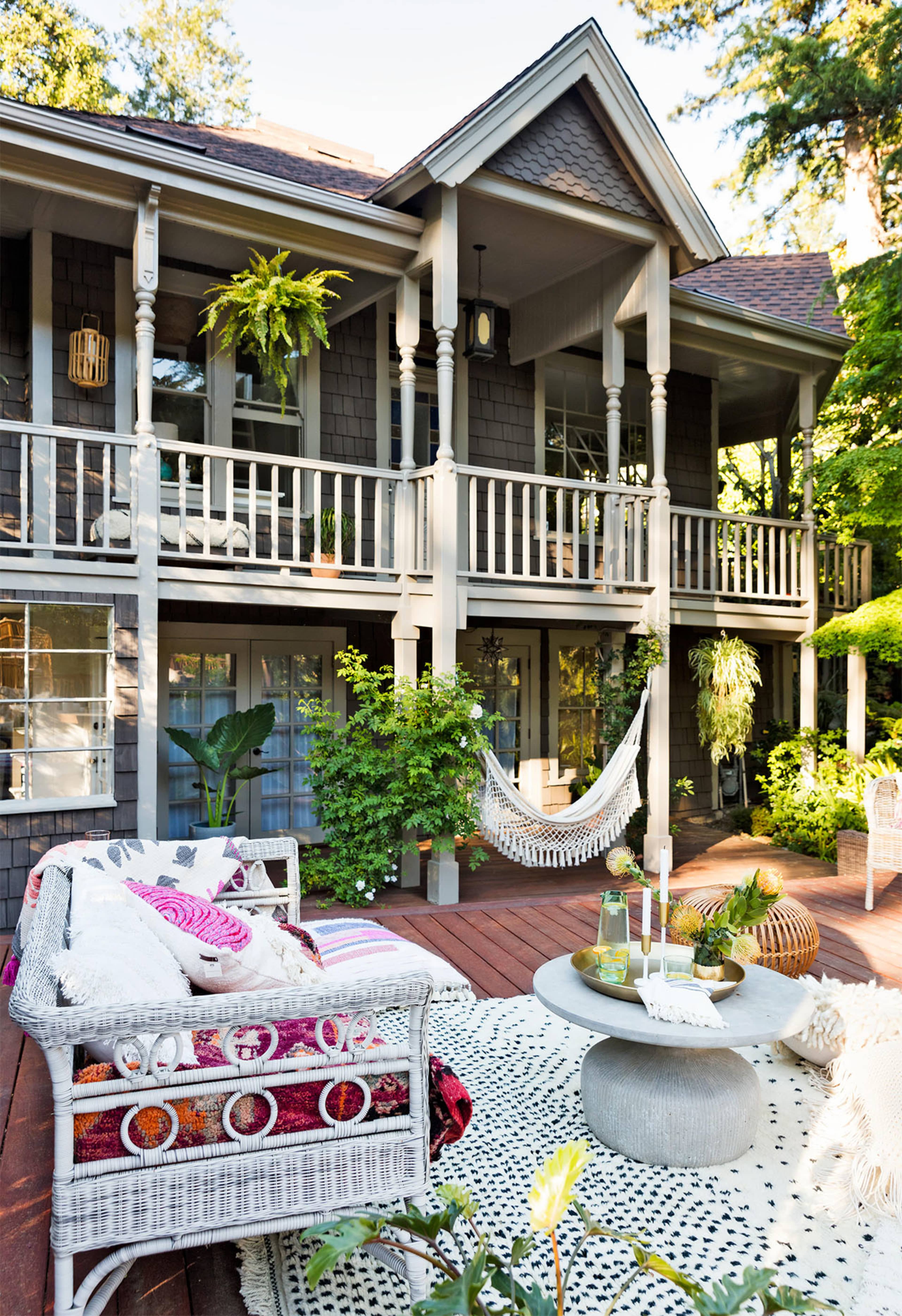 The scene features a cozy outdoor patio with a hammock, comfortable seating, and a central table, surrounded by greenery and a two-story house in the background.