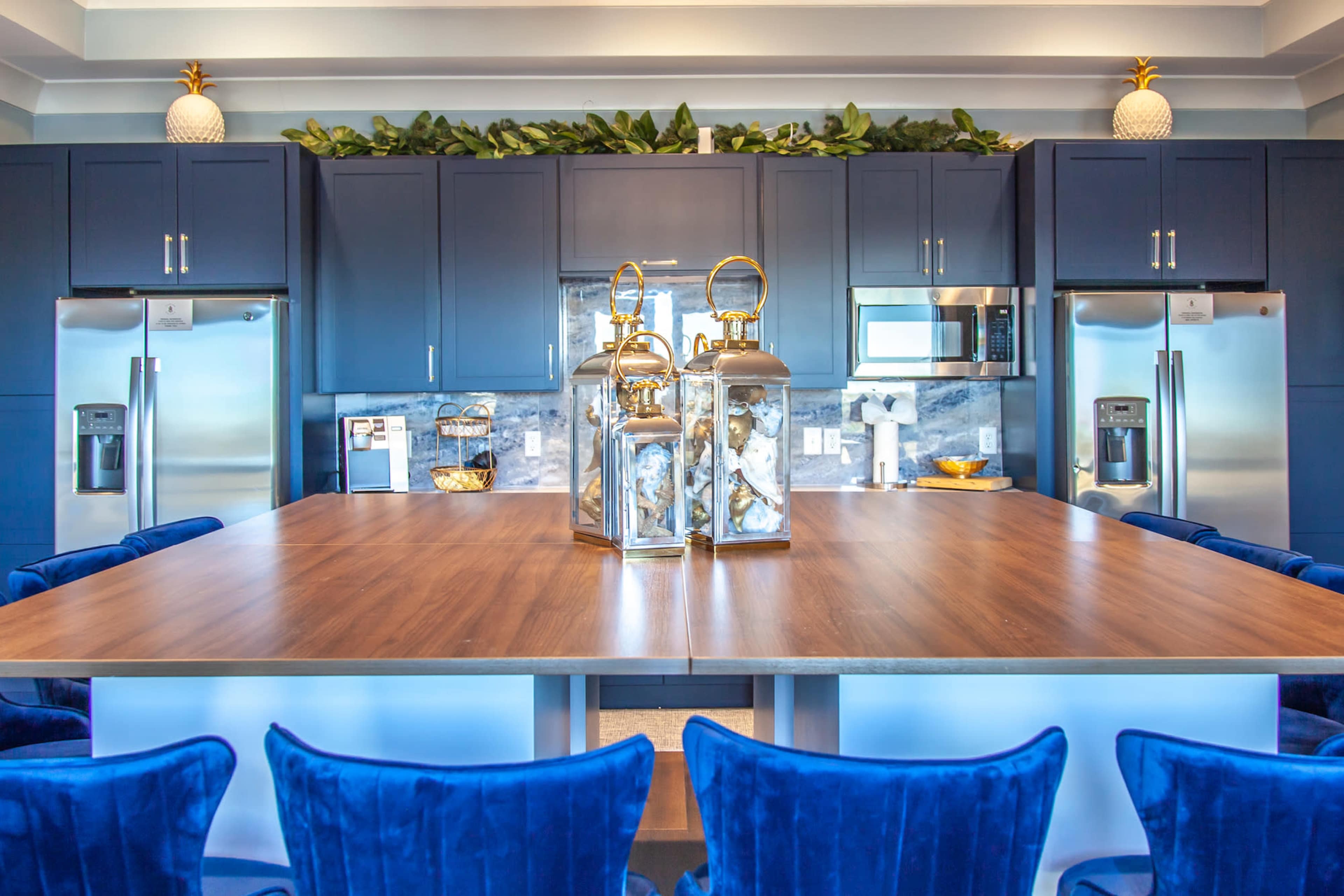 A modern kitchen with dark blue cabinetry, stainless steel appliances, and a central wooden table adorned with decorative lanterns.
