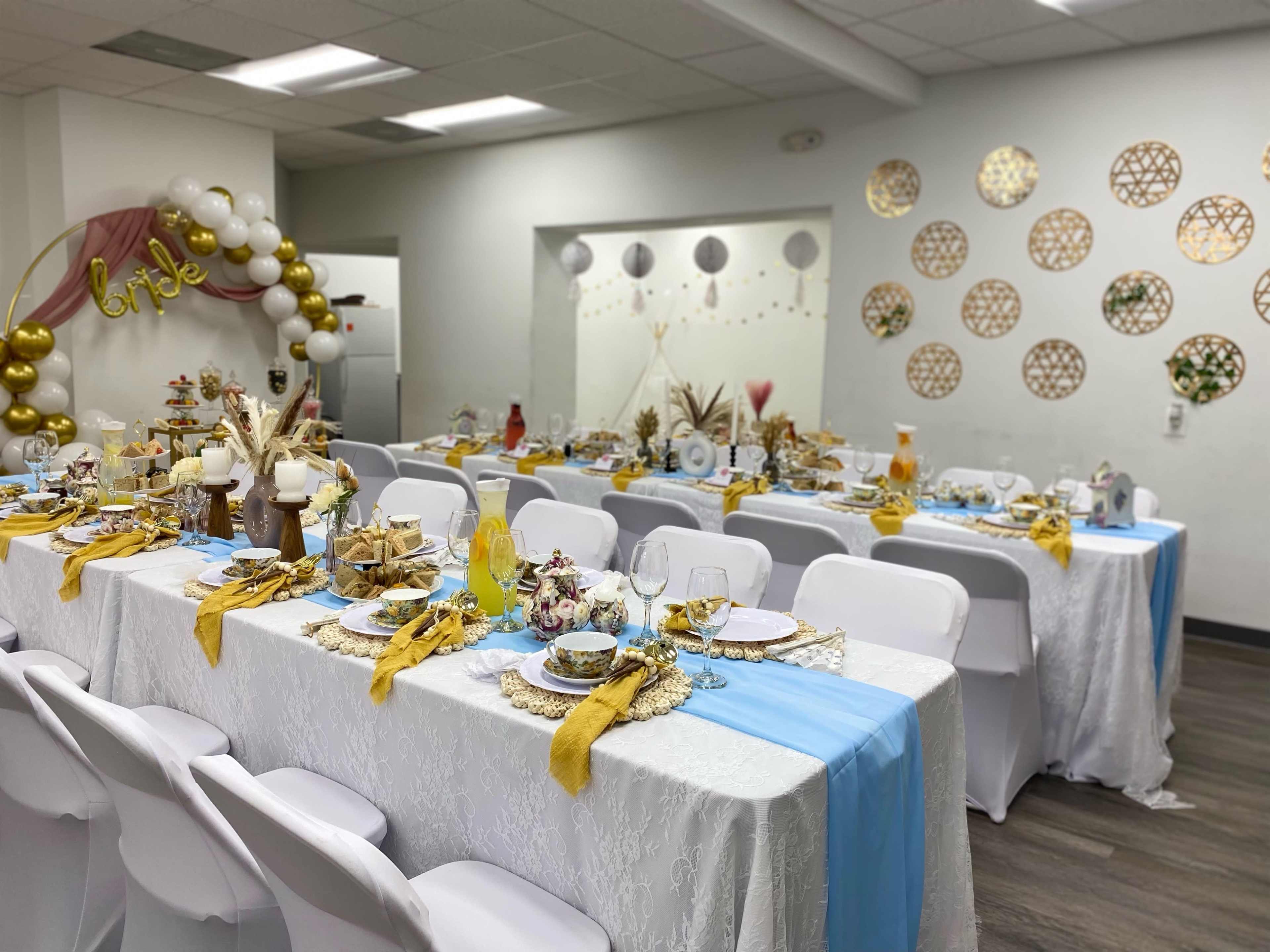 A decorated dining area with elegantly set tables adorned with white tablecloths, gold and blue accents, and decorative centerpieces for an event.
