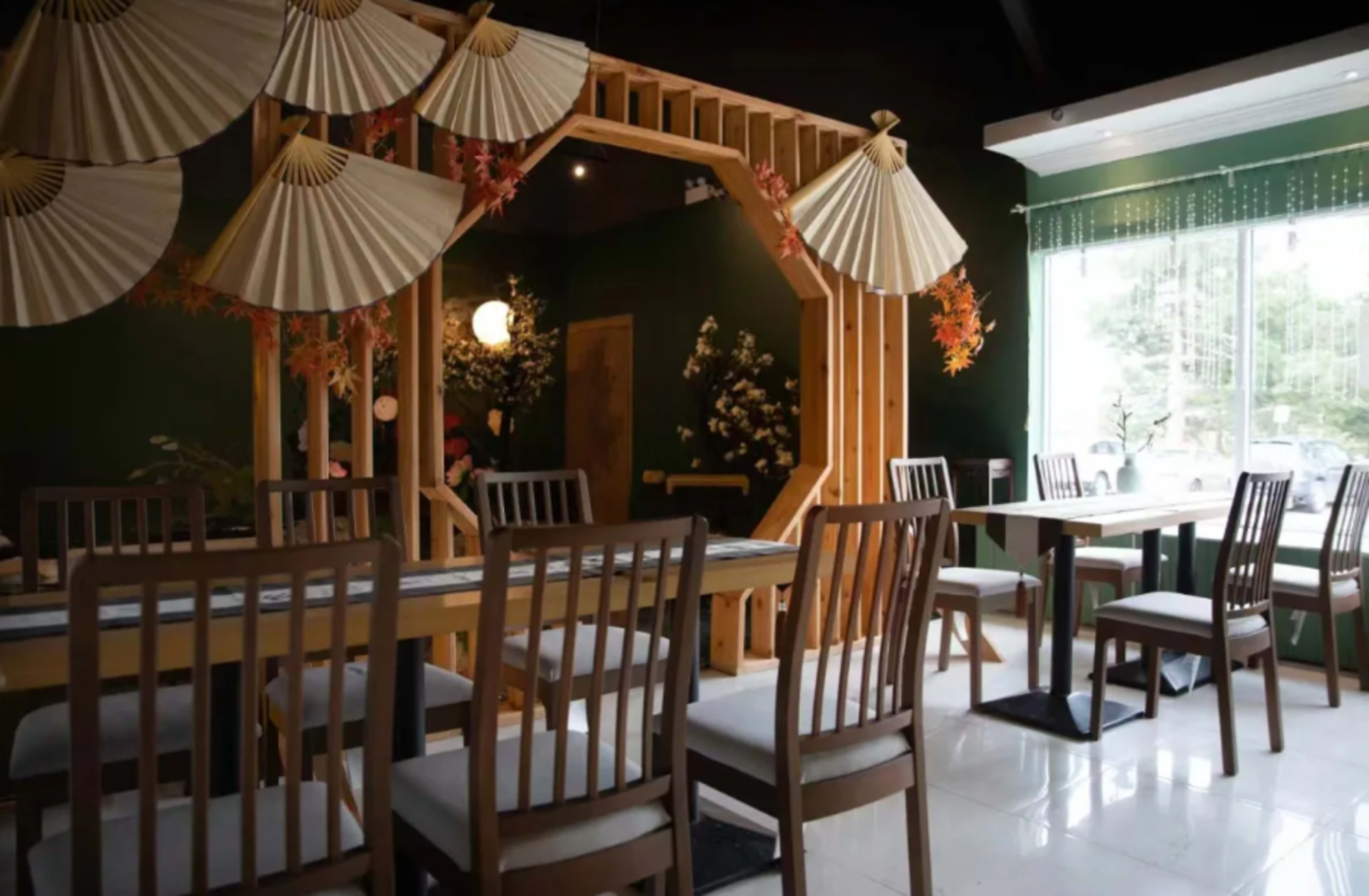 A minimalist dining area features a wooden table surrounded by chairs and decorative fans hanging on the walls.