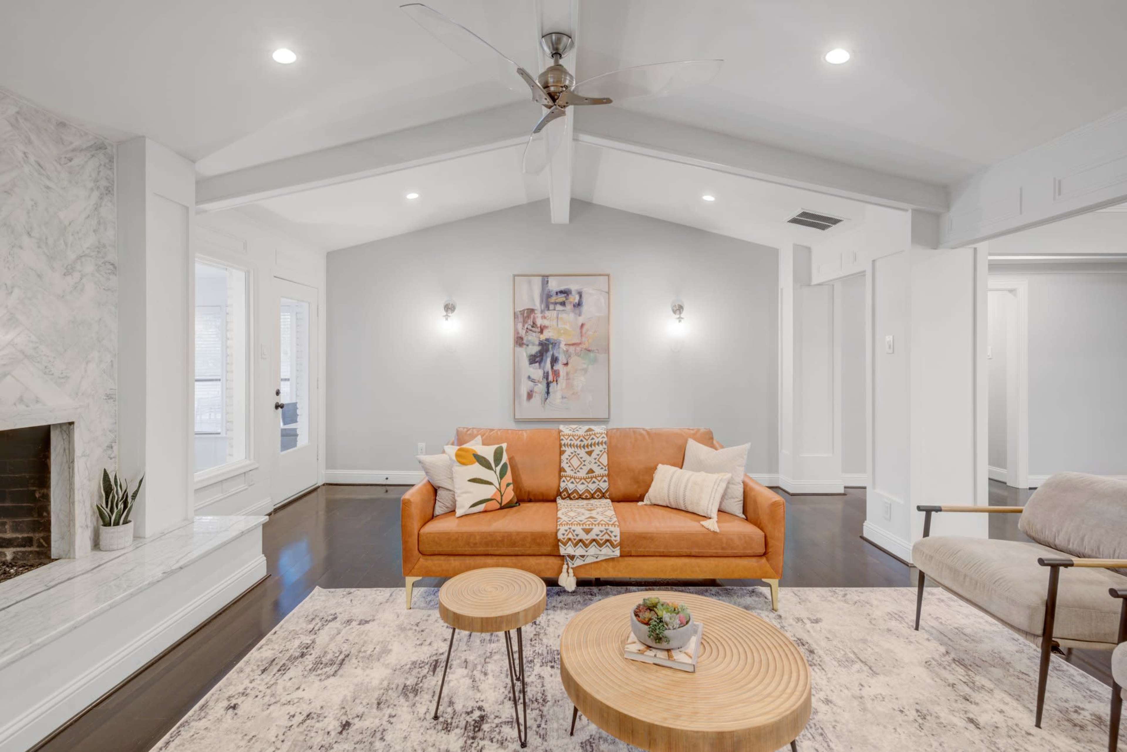 The image features a bright living room with an orange sofa, two wooden coffee tables, and a light-colored rug, complemented by a decorative fireplace and a ceiling fan.