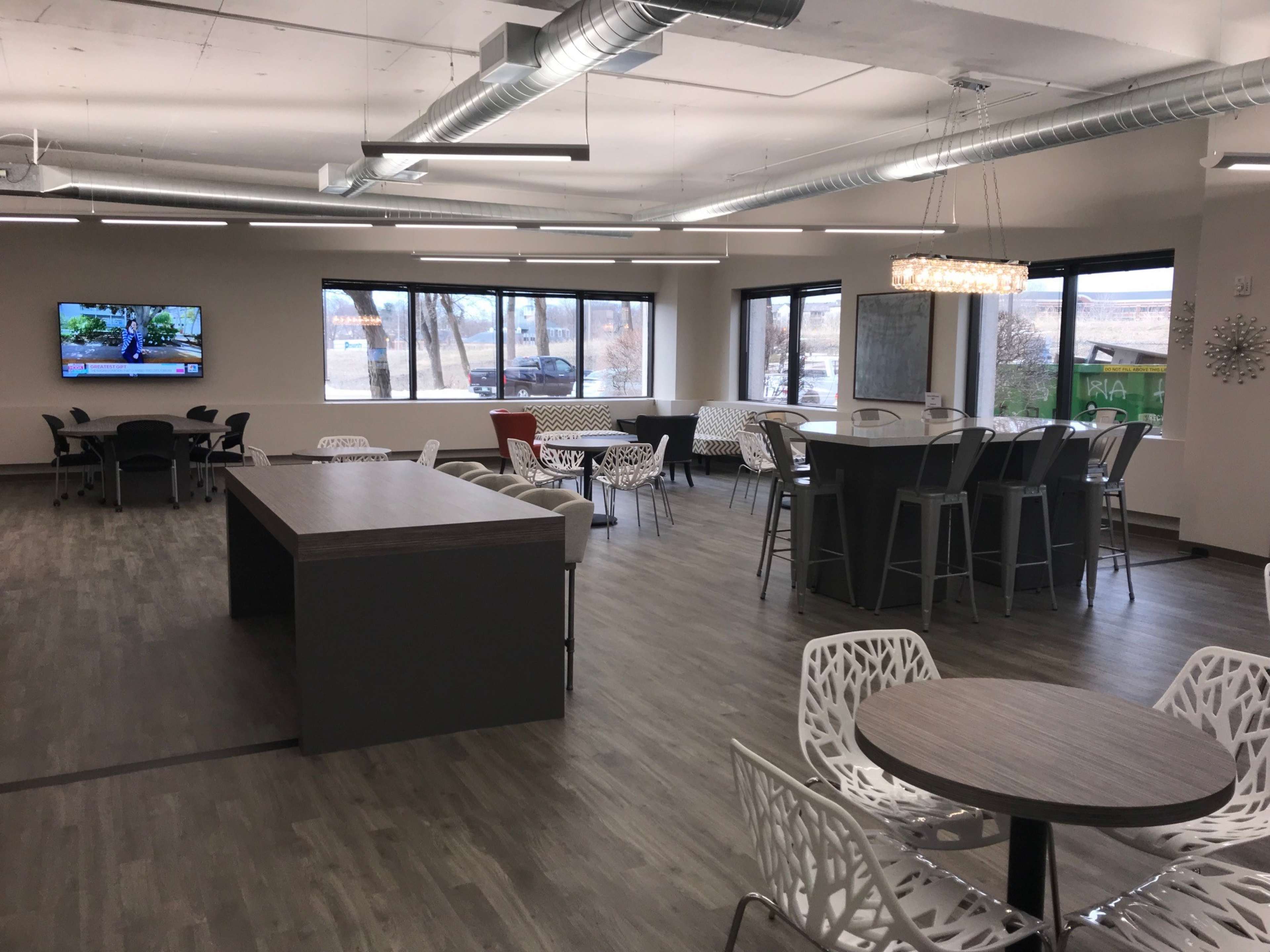 A modern open space with various seating arrangements, including high tables and lounge chairs, accompanied by a television on the wall.