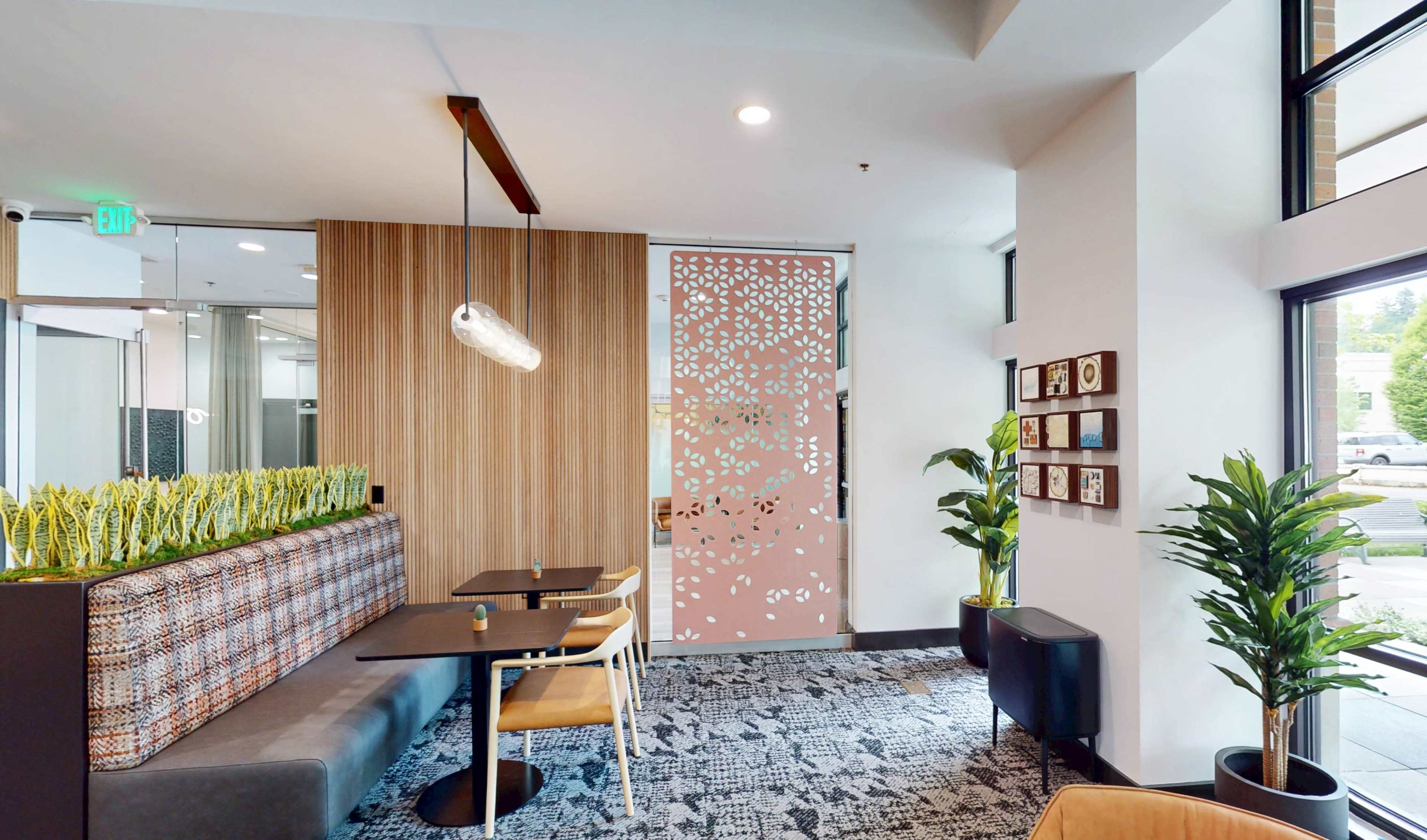 The image shows a modern interior of a cafe-like space with wooden walls, seating areas, and decorative plant elements.