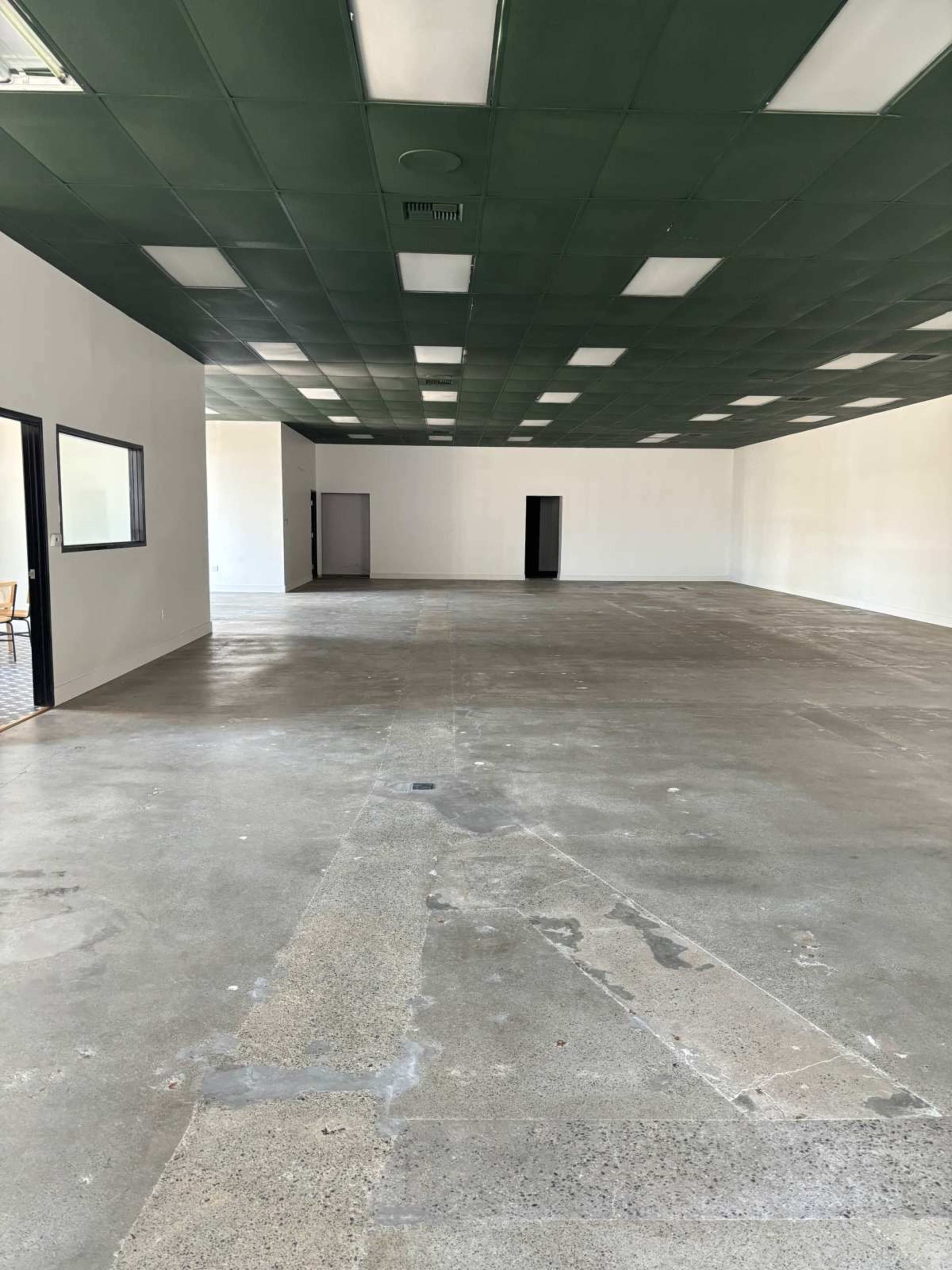 The image shows a large, empty room with a concrete floor, white walls, and a green ceiling.