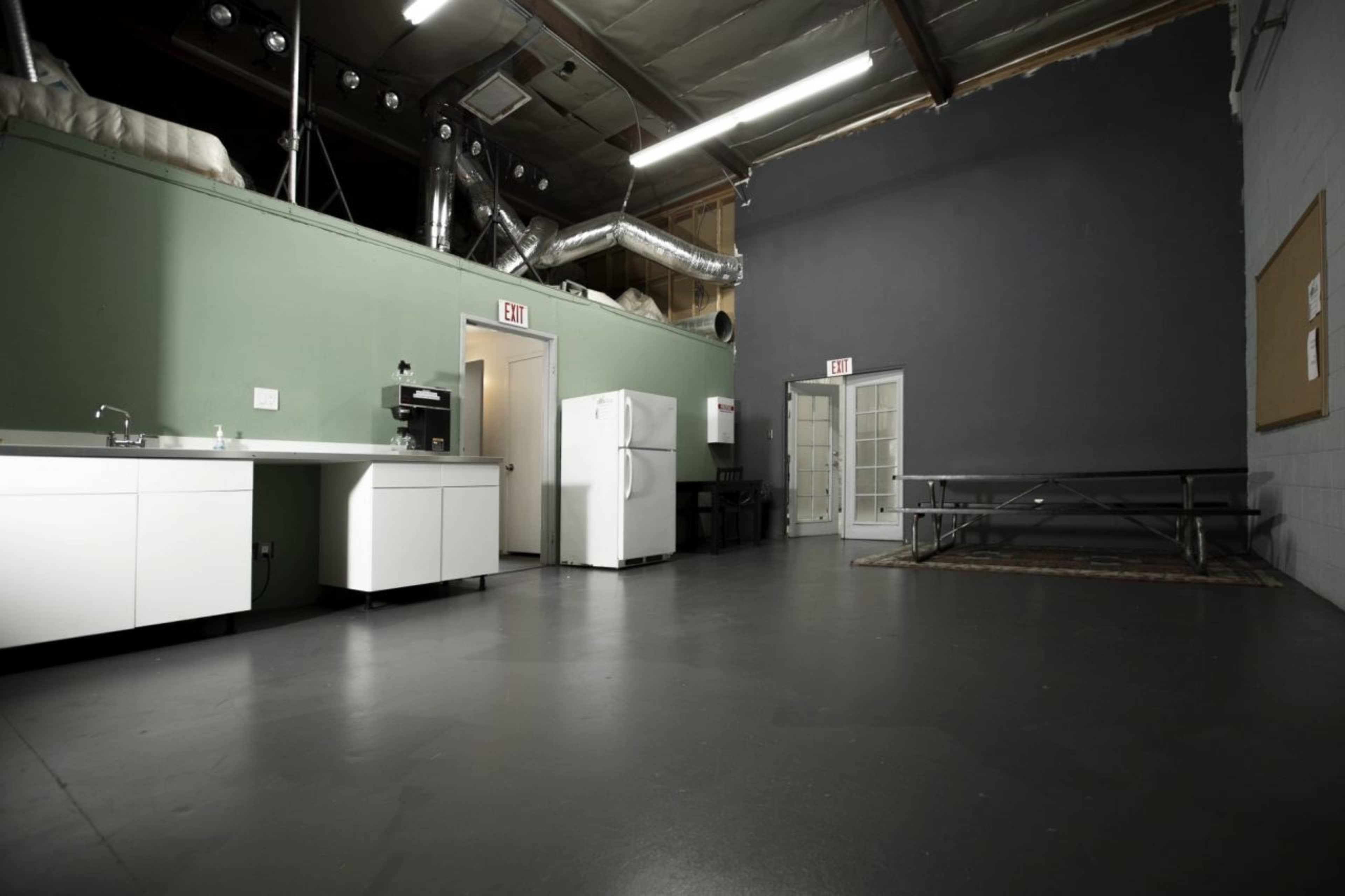 An empty room with a kitchenette on one side, a refrigerator, and a folding table against the wall.