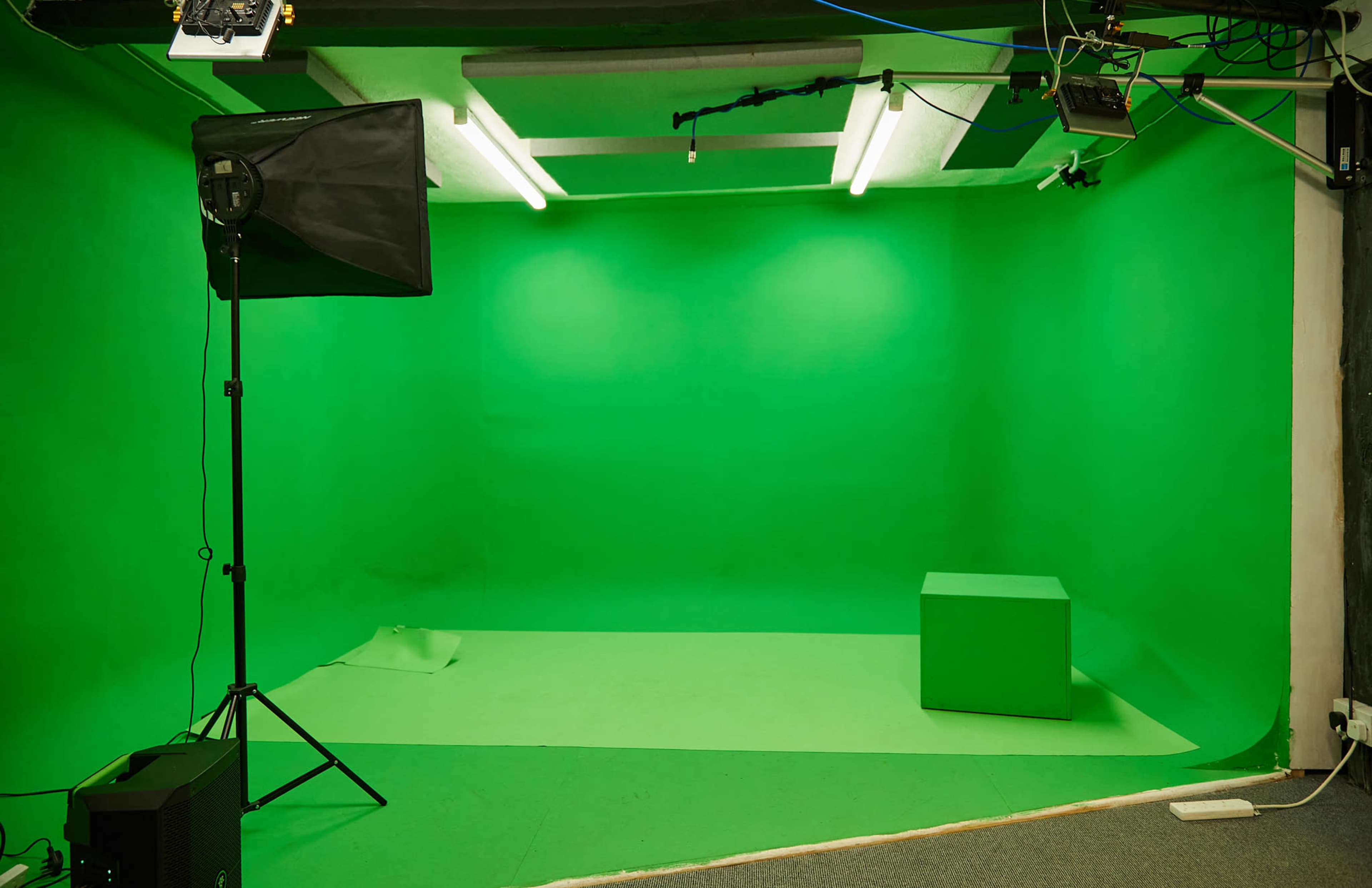 The image shows a green studio backdrop with a light set up and a single green cube on the floor.
