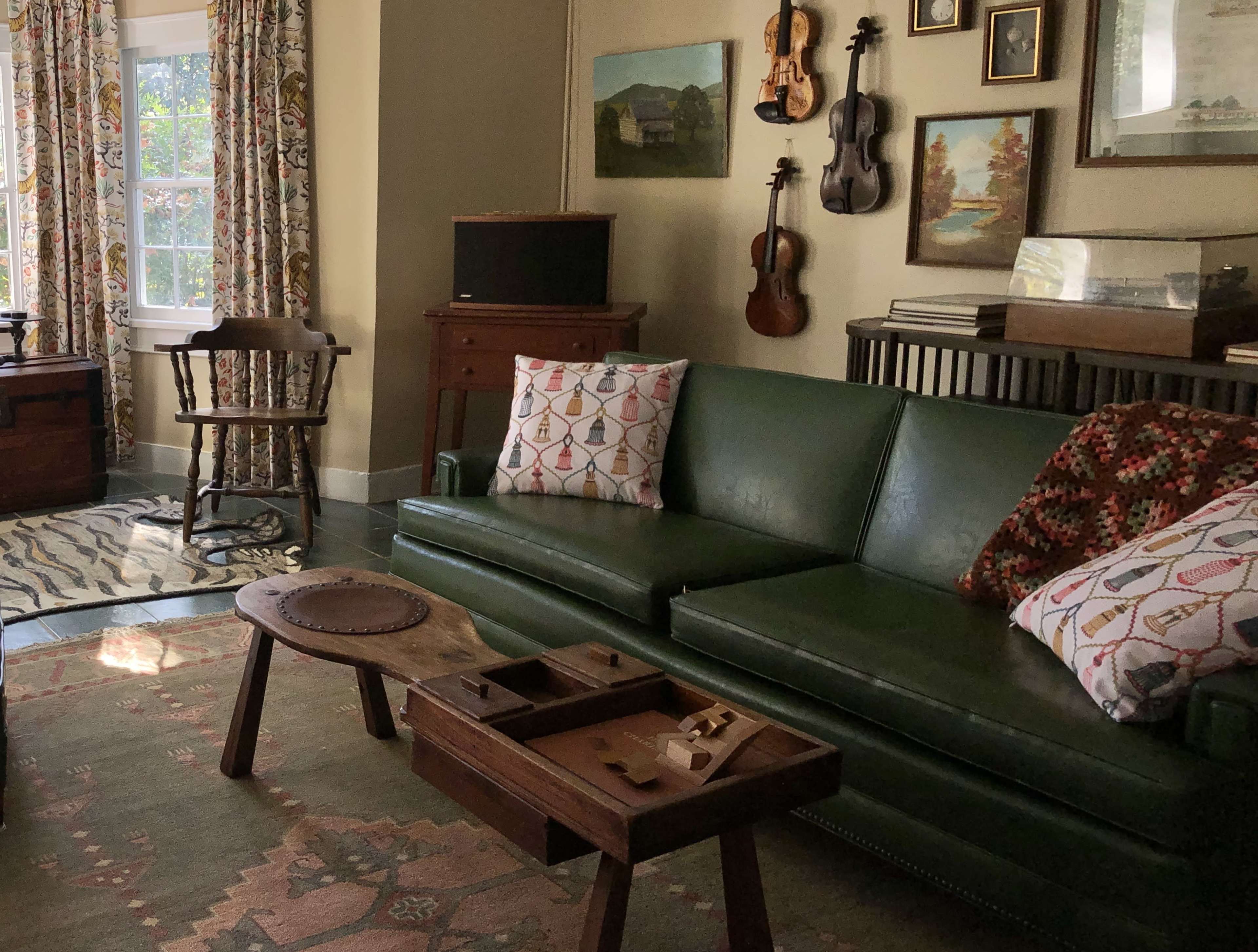 The living room features a green sofa with patterned pillows, a wooden coffee table with a compartment, and vintage decor including framed pictures and musical instruments on the walls.