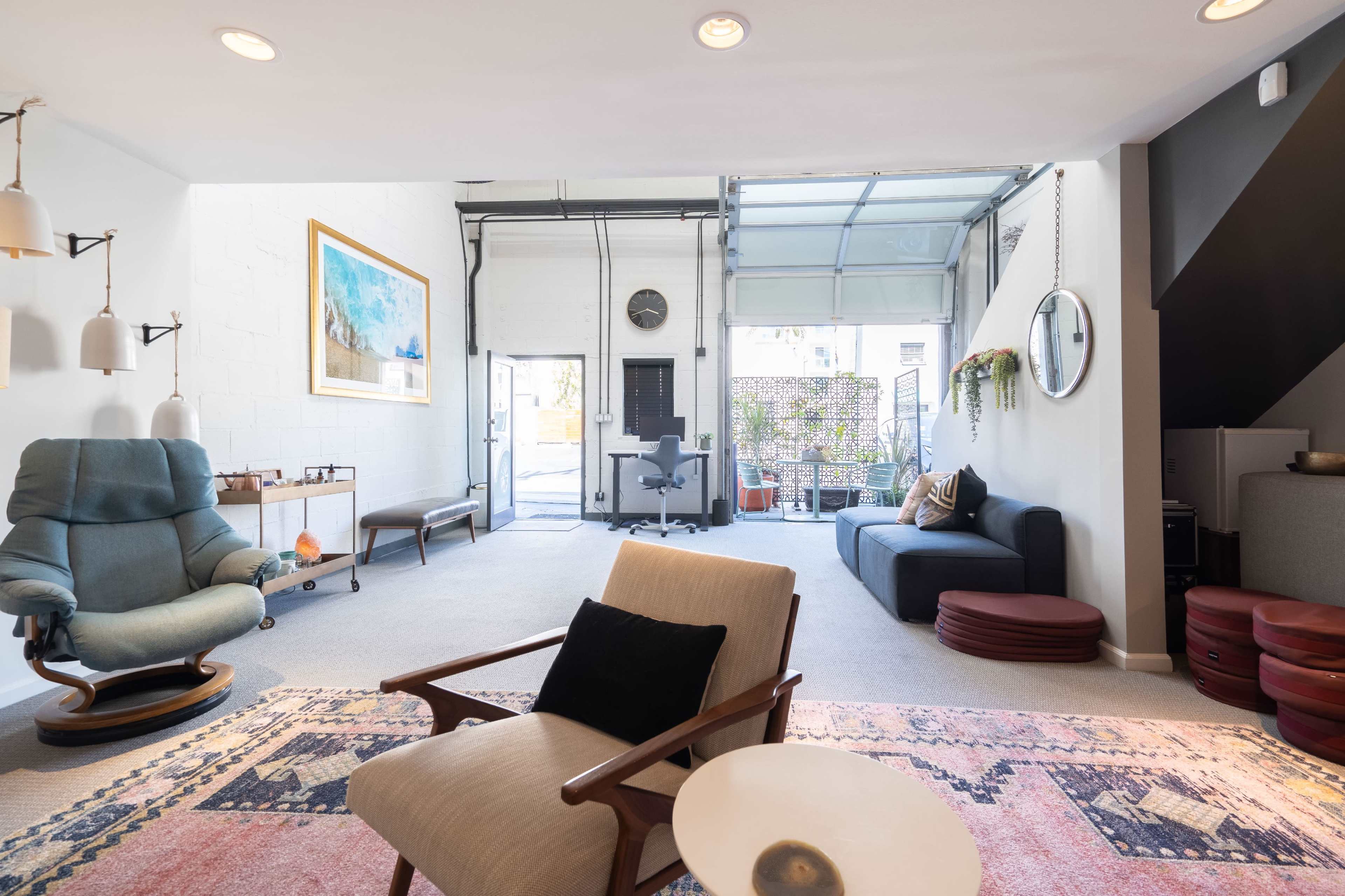 A spacious living area features modern furniture, a large wall art piece, and an open garage door leading to a patio.