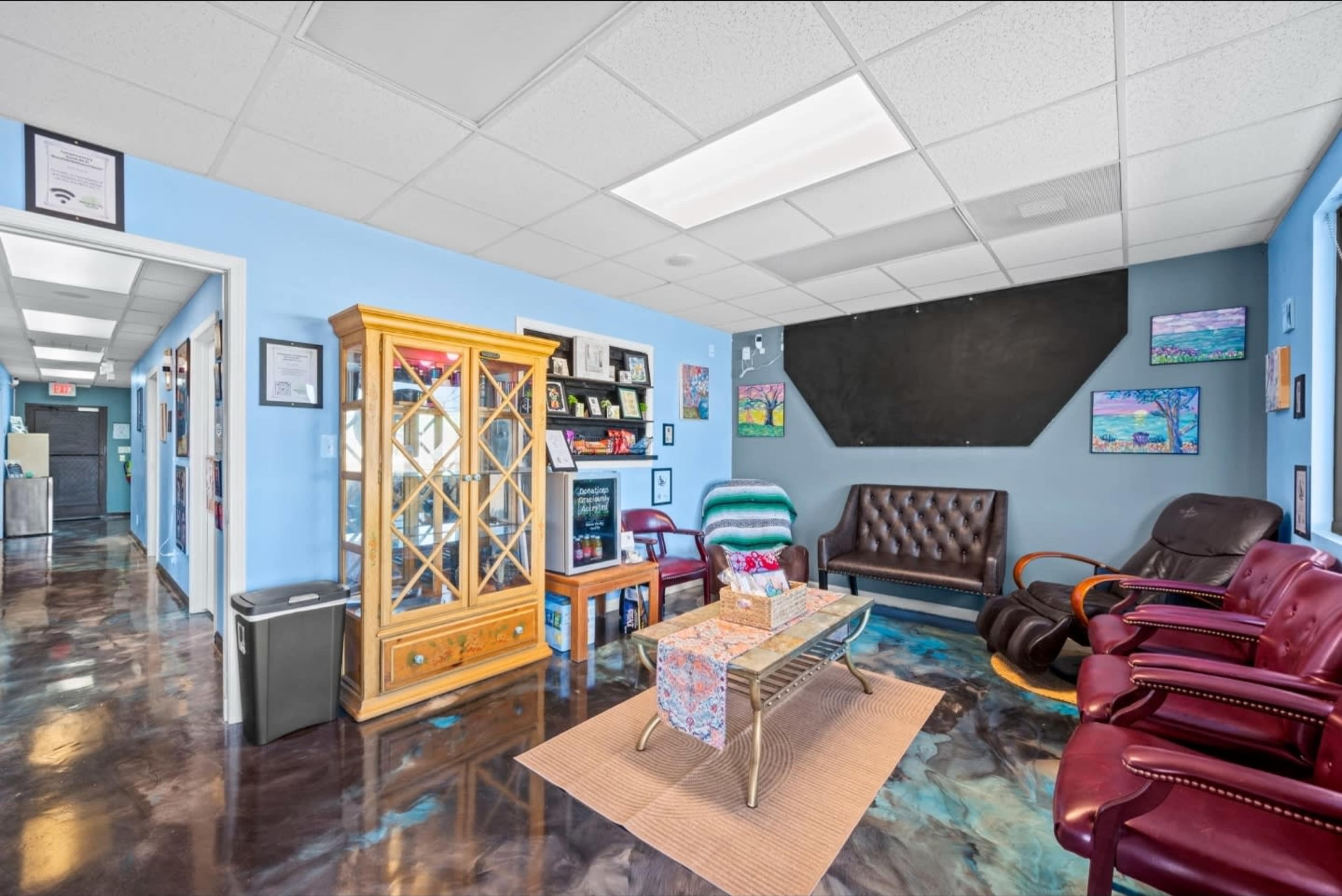 The image shows a waiting area with colorful walls, a mix of seating options, a wooden display cabinet, and artwork on the walls.