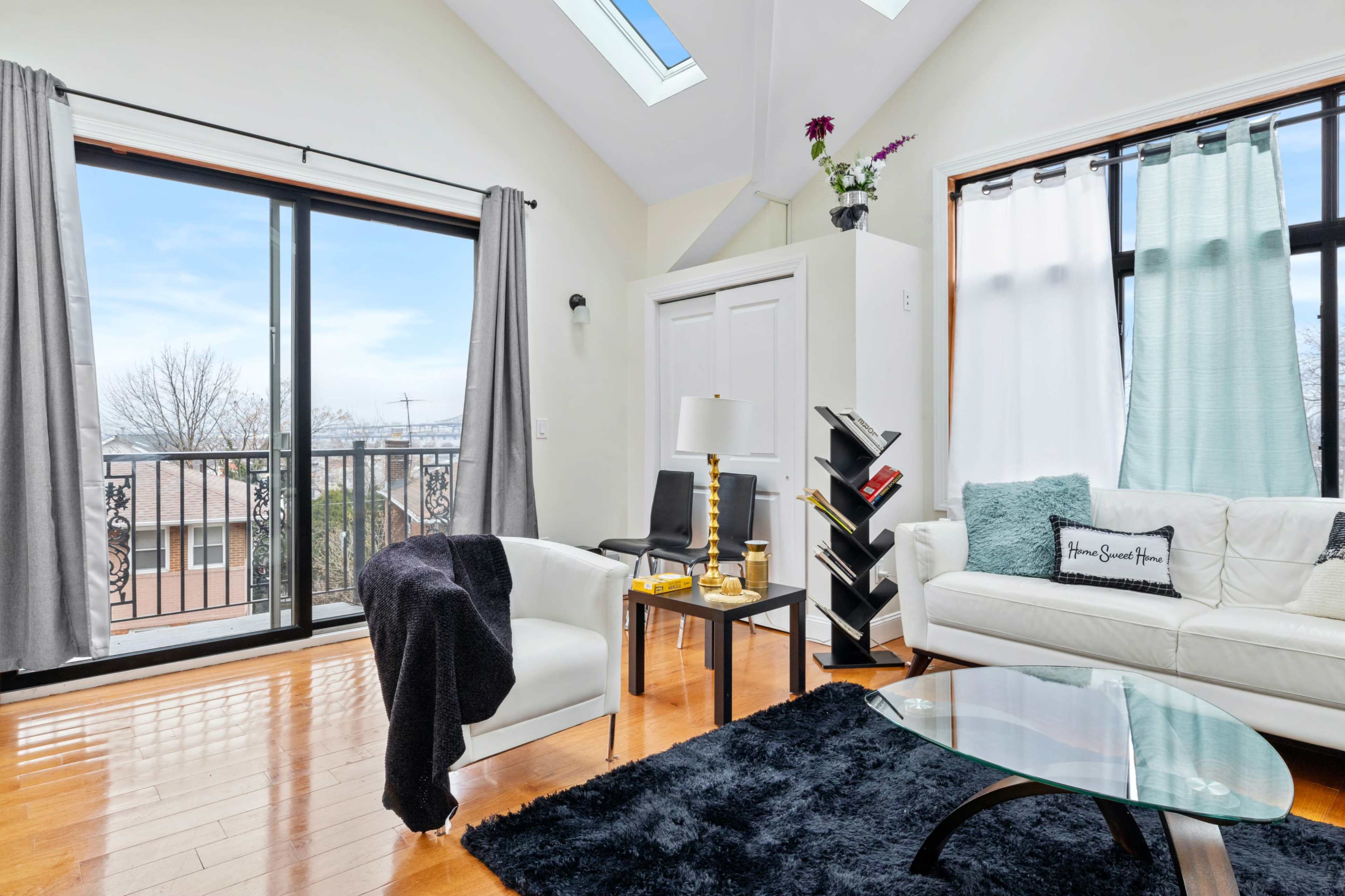 A well-lit living room features large windows, a sliding glass door, a white sofa, a black rug, and a modern coffee table.