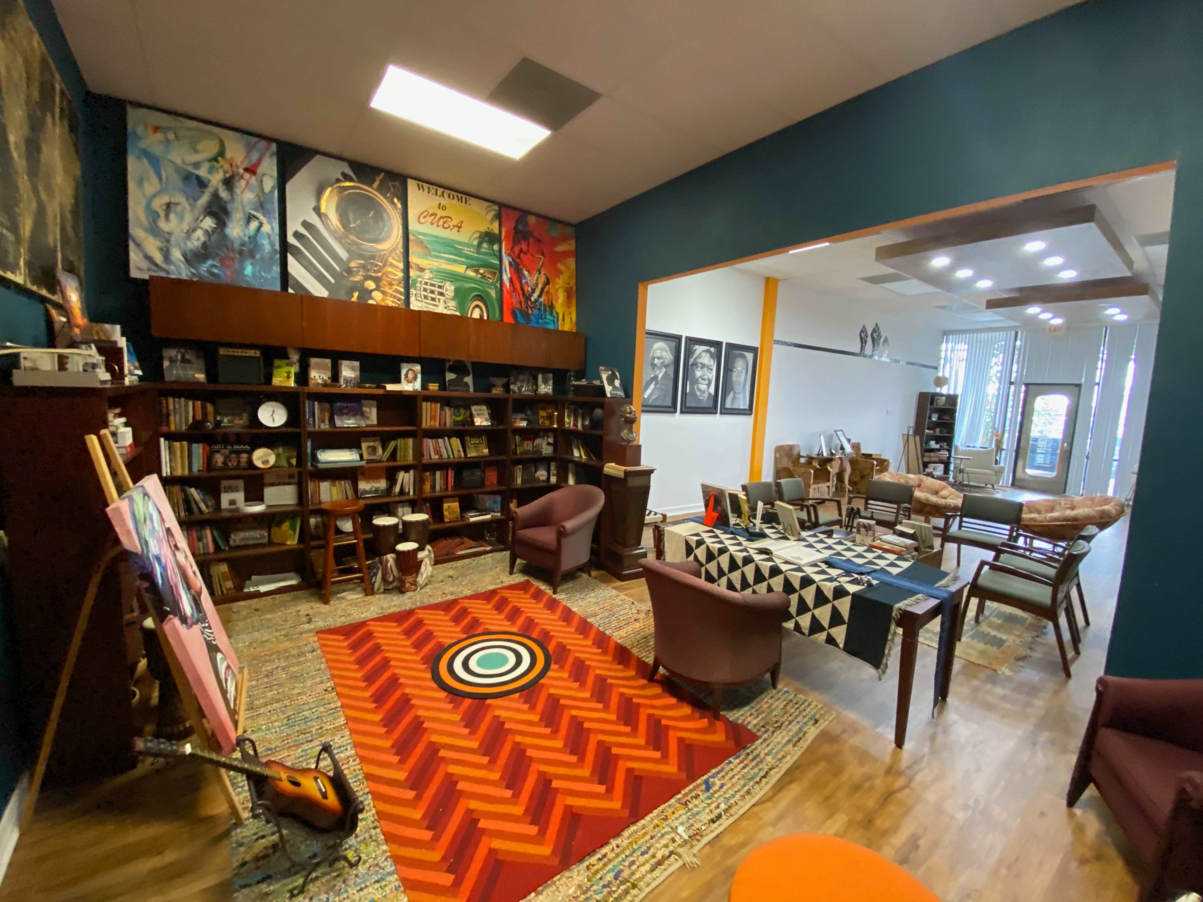 The image shows a cozy lounge area with bookshelves, seating, and colorful rugs, creating an inviting space for reading and relaxation.