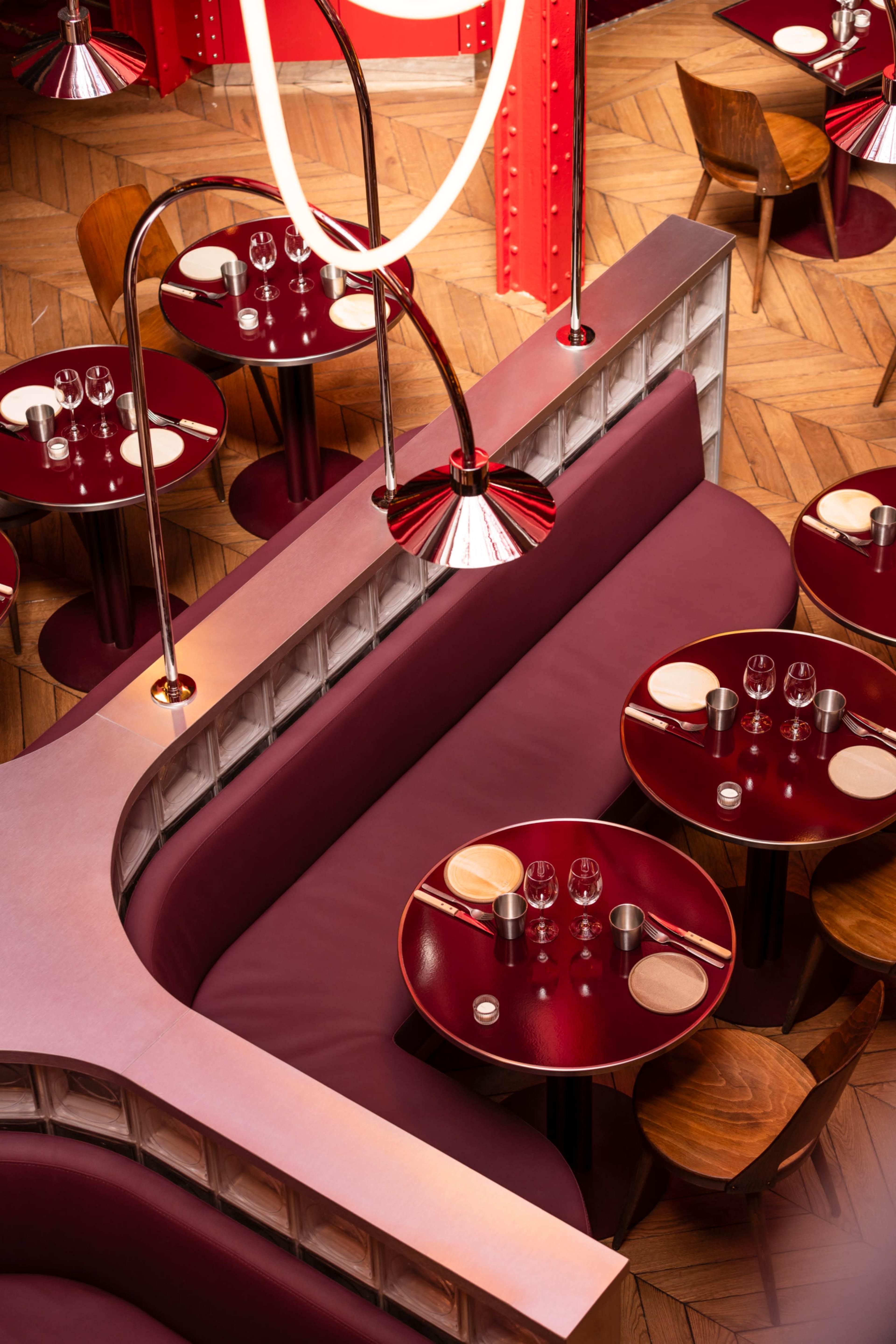 The image features a modern restaurant interior with several circular tables set for dining, surrounded by burgundy booths and light fixtures.