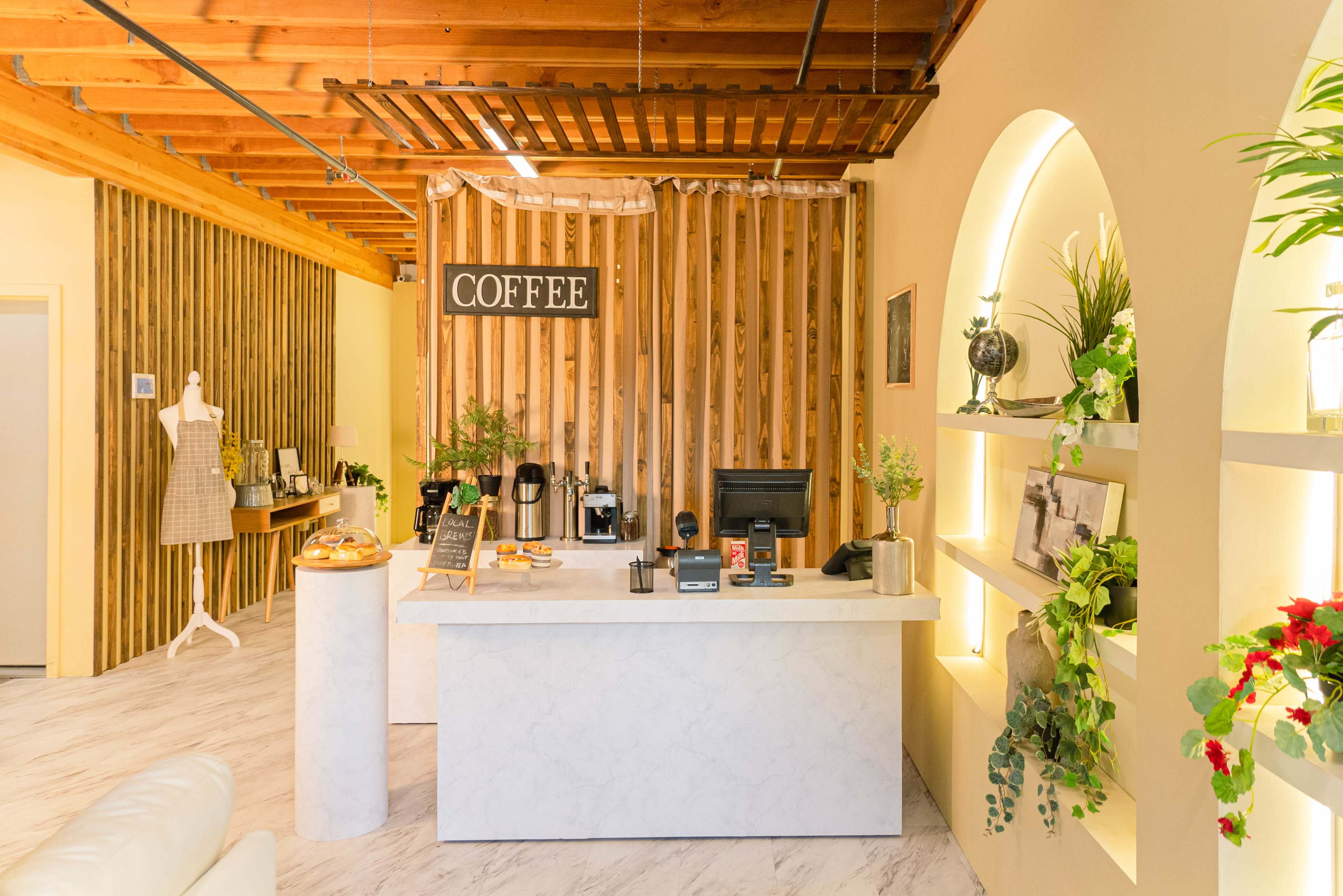 The image displays a modern coffee shop interior with a marble counter, wooden paneling, and decorative plants on shelves.