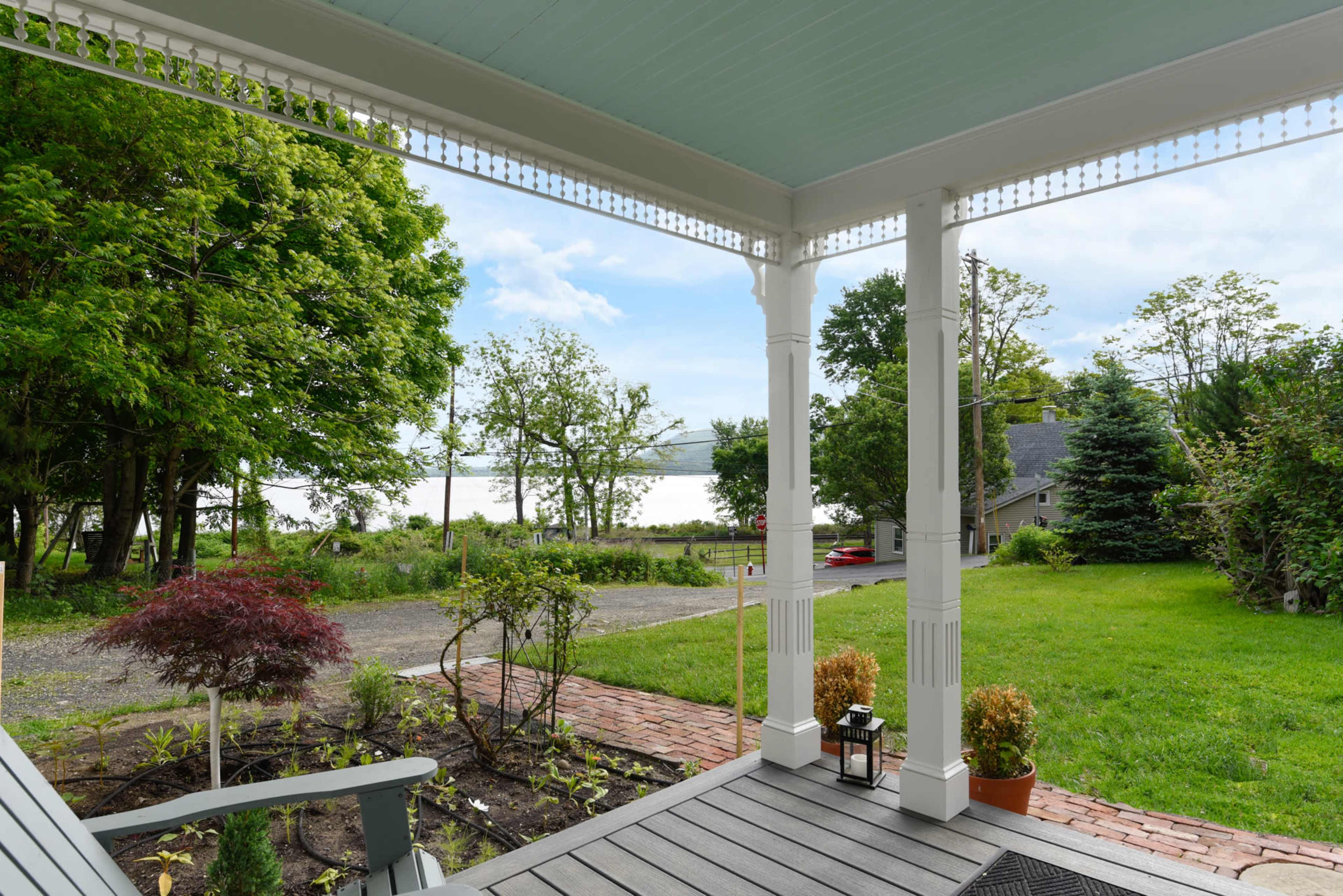 The image shows a porch view overlooking a grassy yard with trees and a distant body of water.