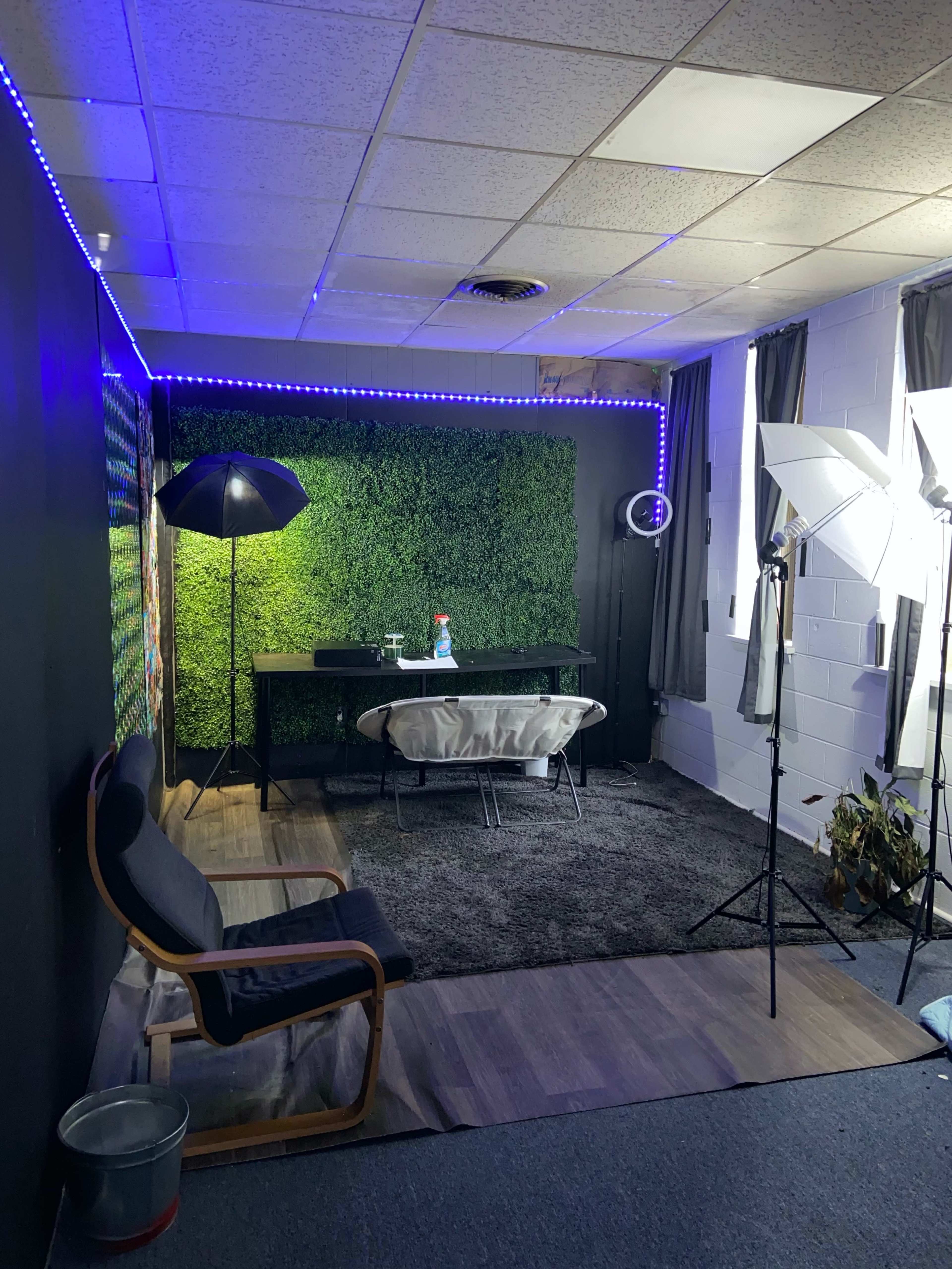A small studio space with a green wall, a black desk, and photography lighting equipment.