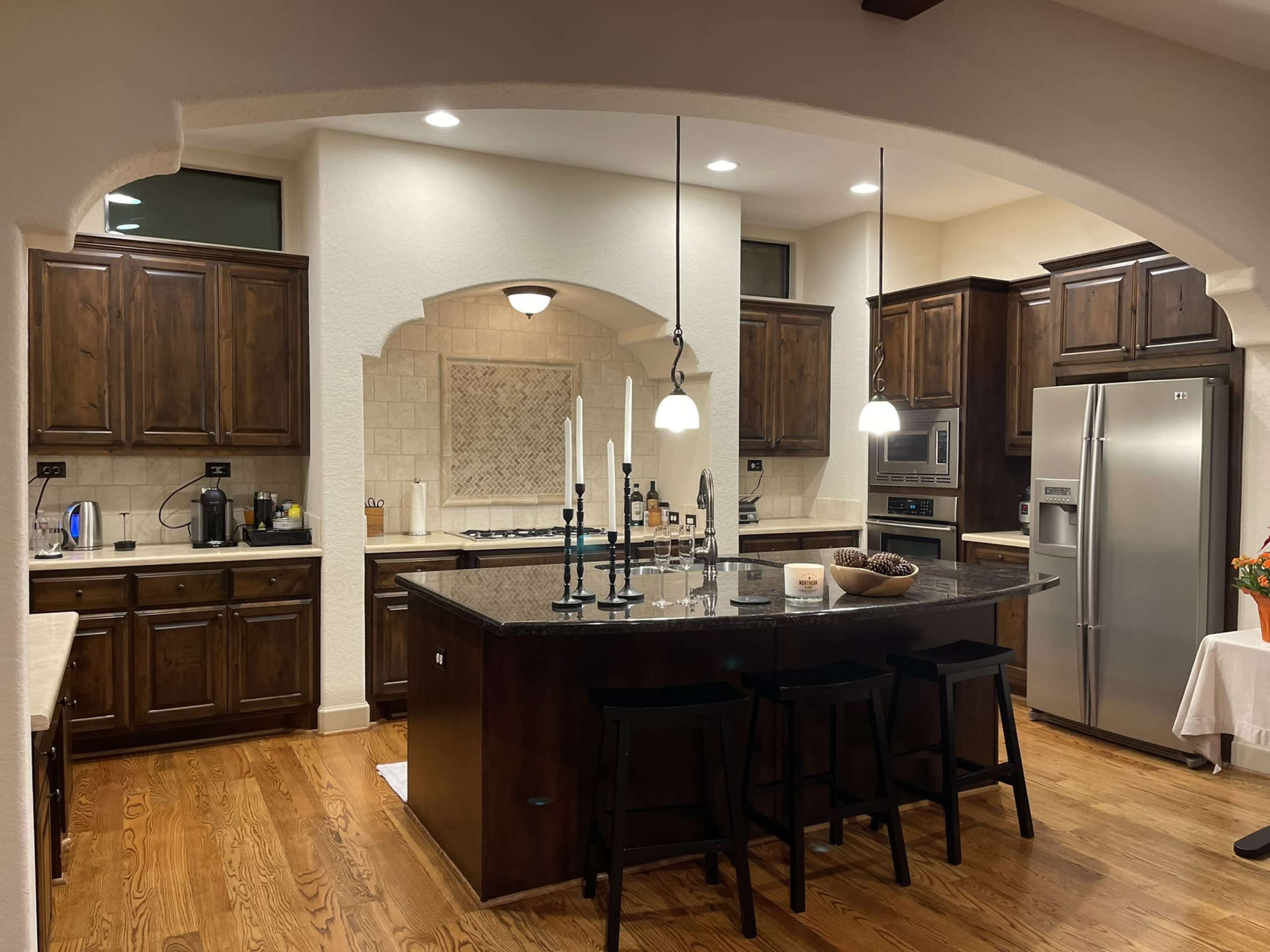 A modern kitchen featuring dark wooden cabinets, a large central island with seating, stainless steel appliances, and a well-lit area with decorative candles.
