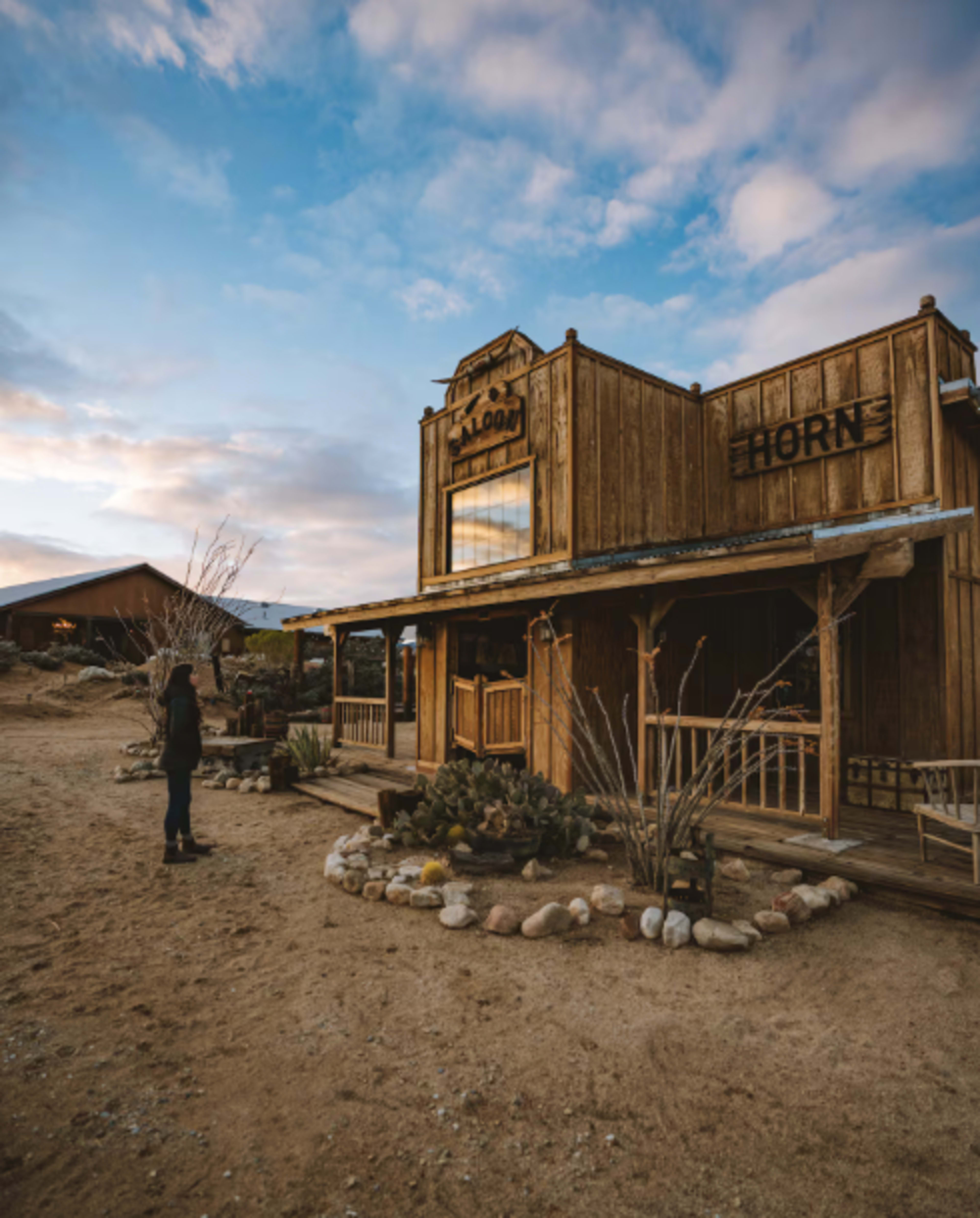 A wooden saloon with a sign reading "HORN" stands in a desert landscape under a cloudy sky.