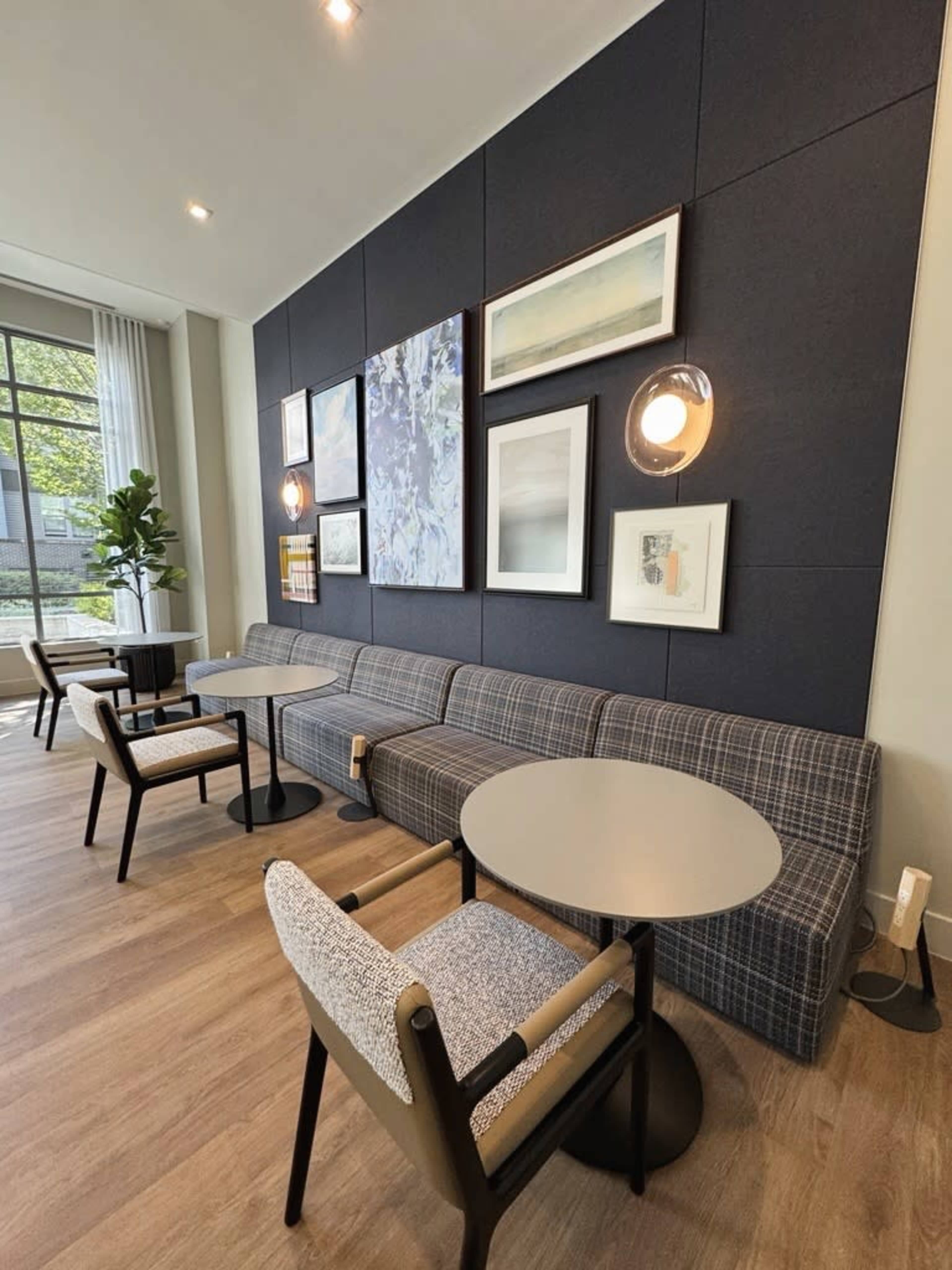 The image shows a modern cafe interior featuring a gray upholstered bench, round tables, and artwork displayed on the wall.