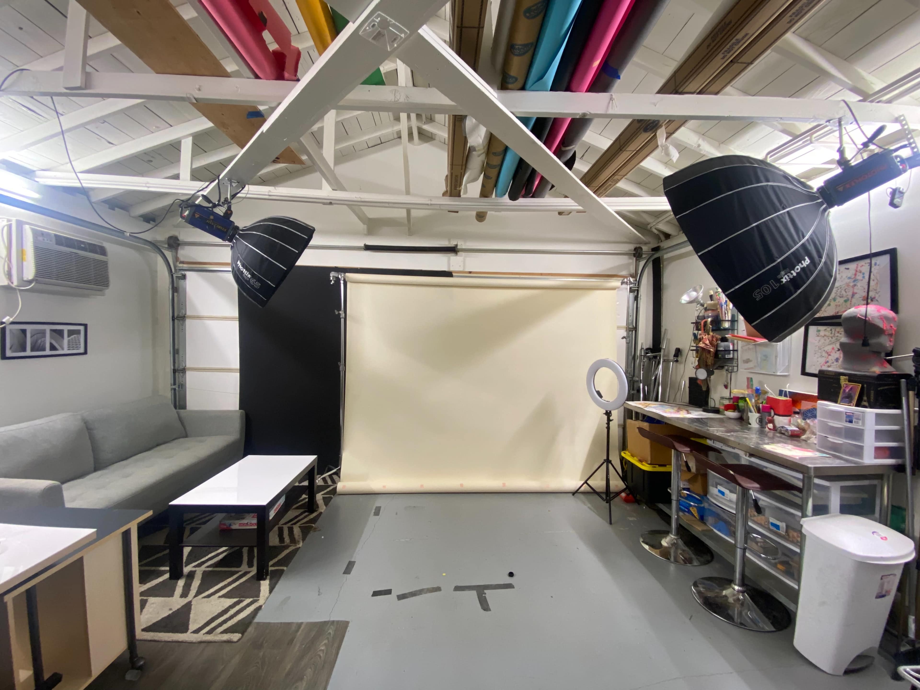 A photography studio with a light backdrop, two large softbox lights, a couch, and a table.