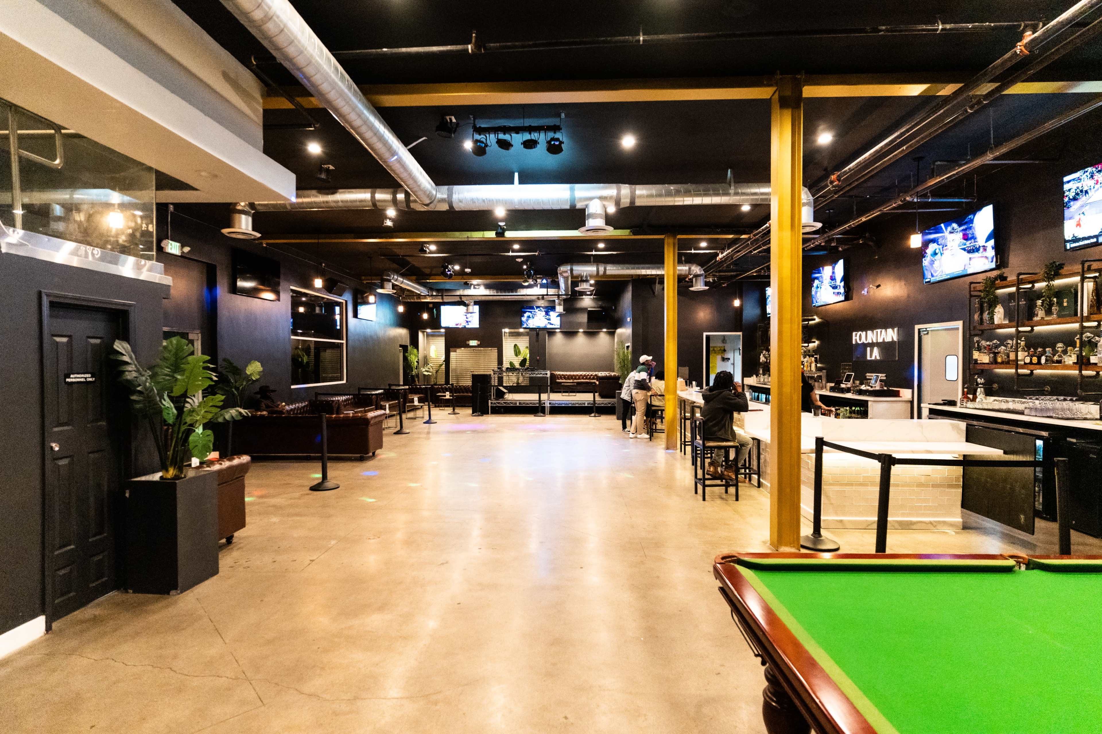 A spacious lounge area with a bar, pool table, and several seating arrangements, along with multiple screens mounted on the walls.