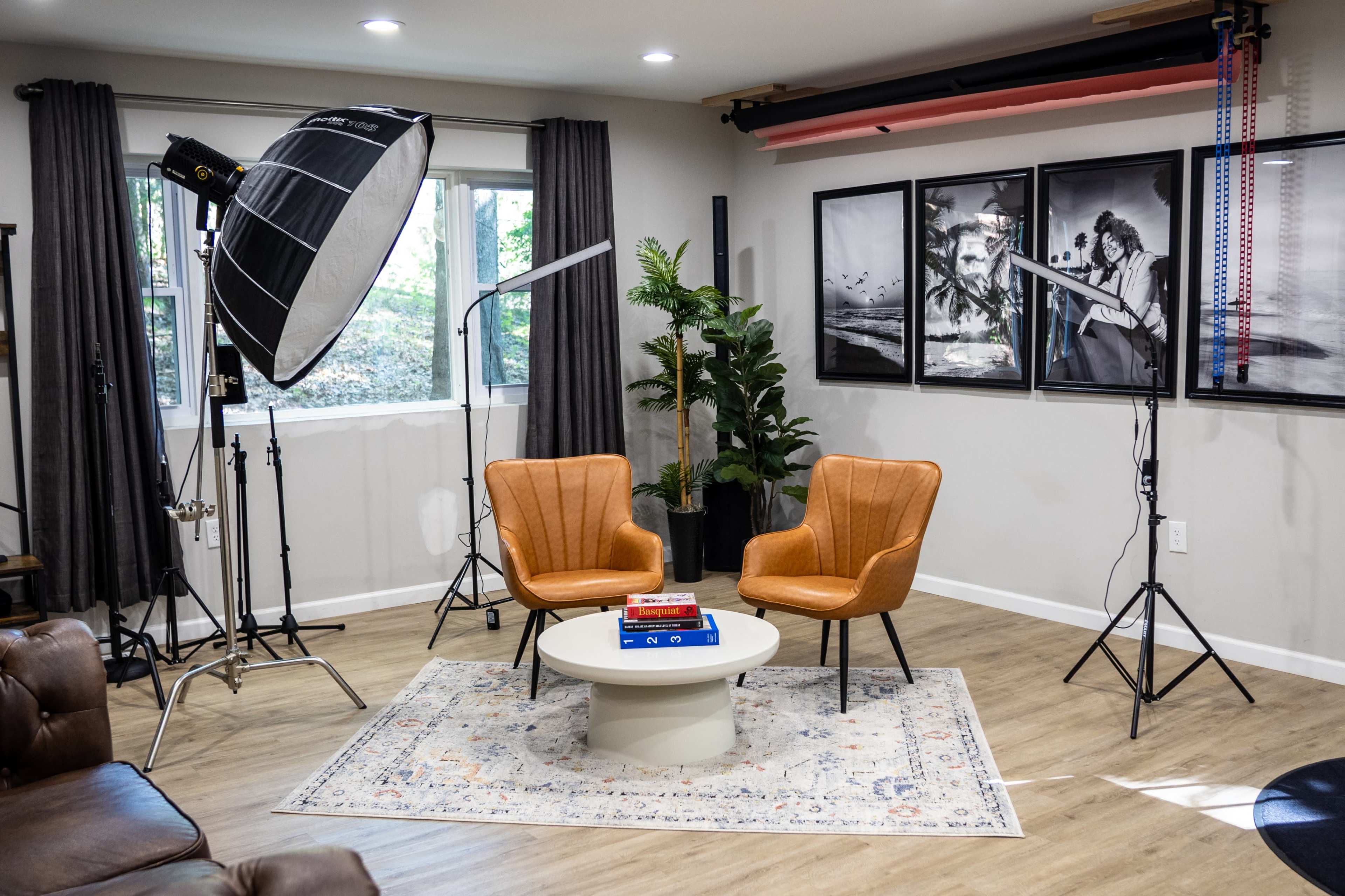 A modern studio setting with two orange chairs and a round table, surrounded by lighting equipment and framed photographs on the wall.
