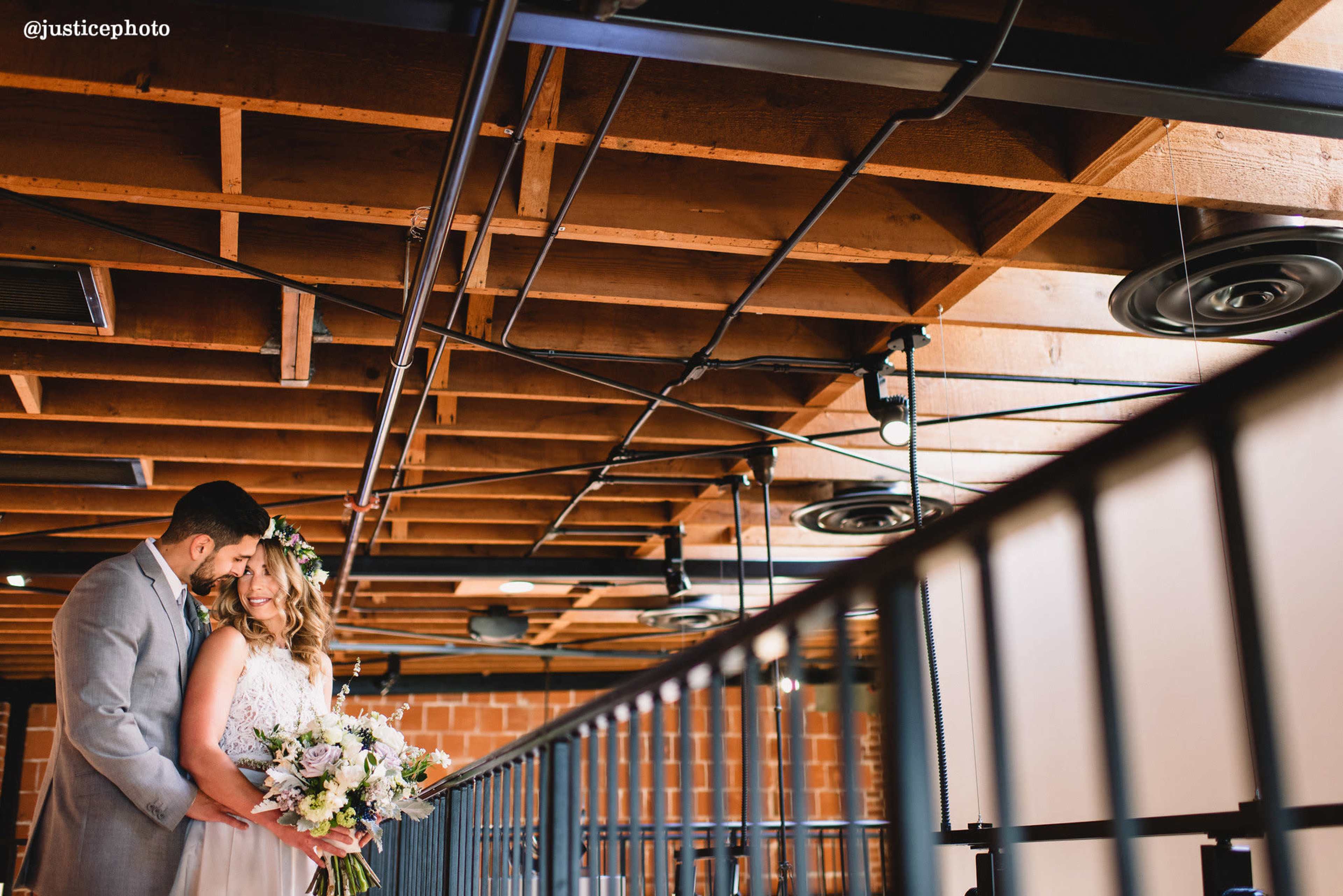 A couple embraces on a balcony under a wooden ceiling, holding a bouquet of flowers.