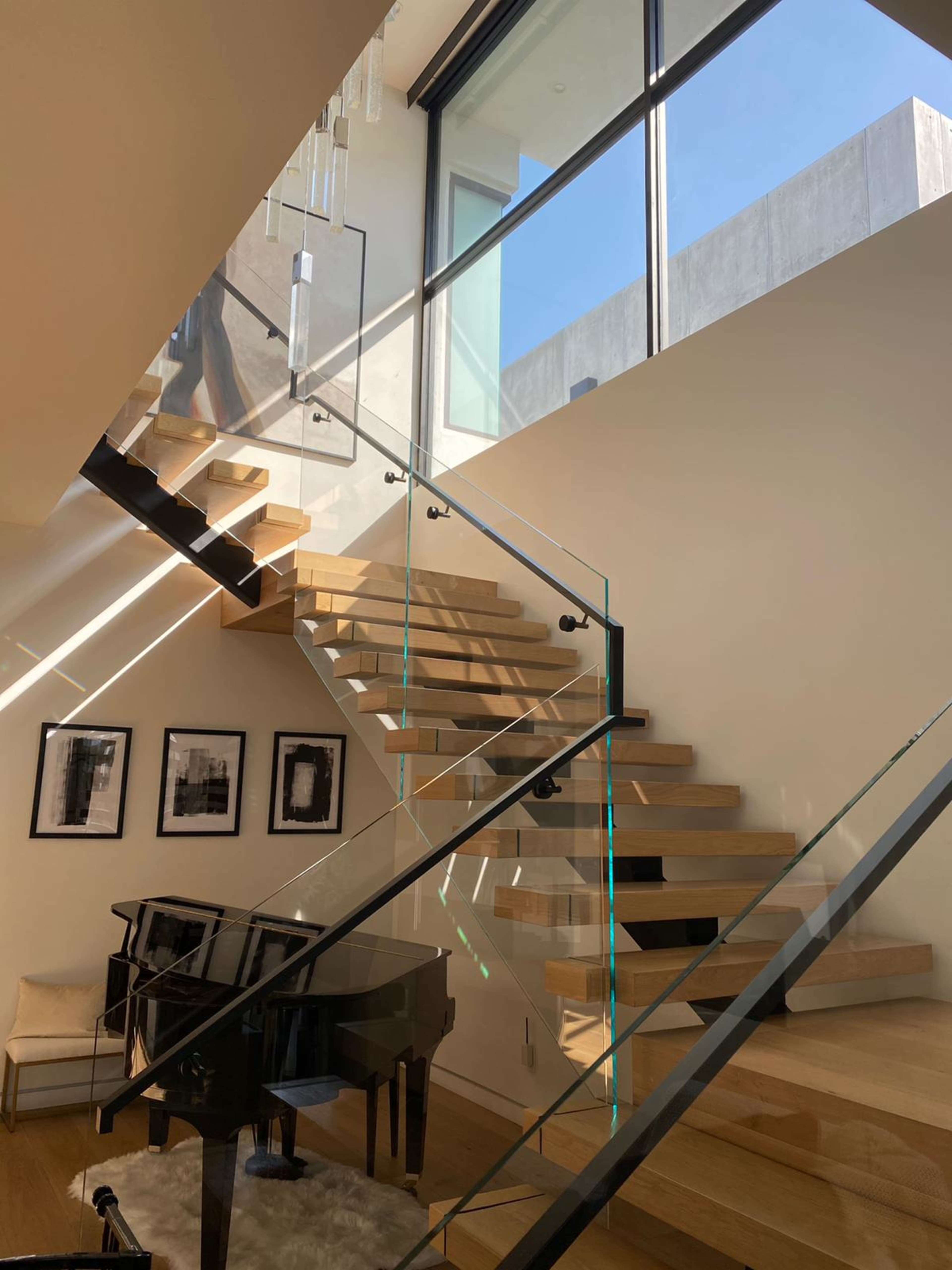 A modern staircase with wooden steps and glass railings, leading up to a large window in a bright interior space.