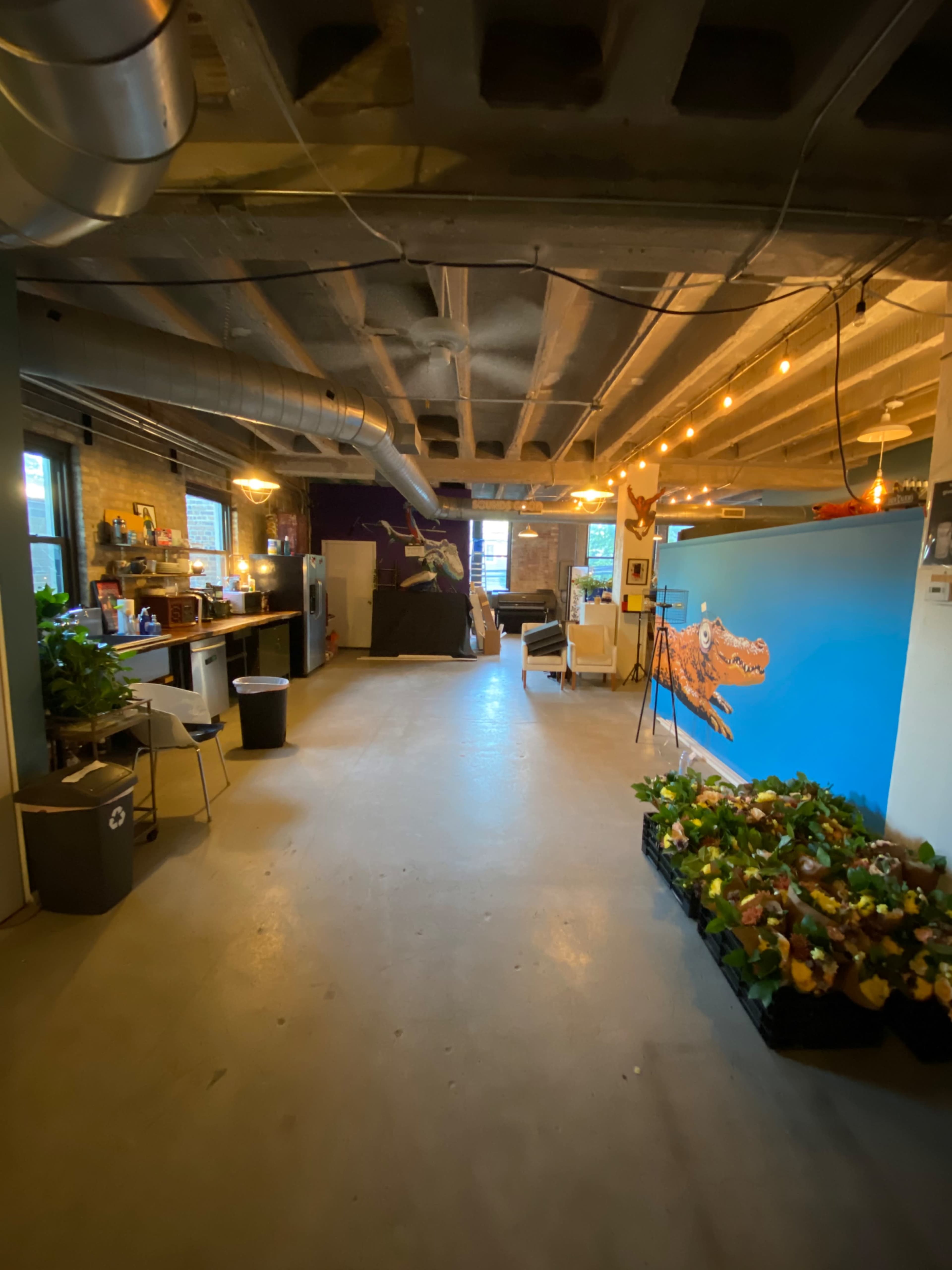 A spacious, well-lit office area featuring plants, artwork on the walls, and a seating area with various furniture items.