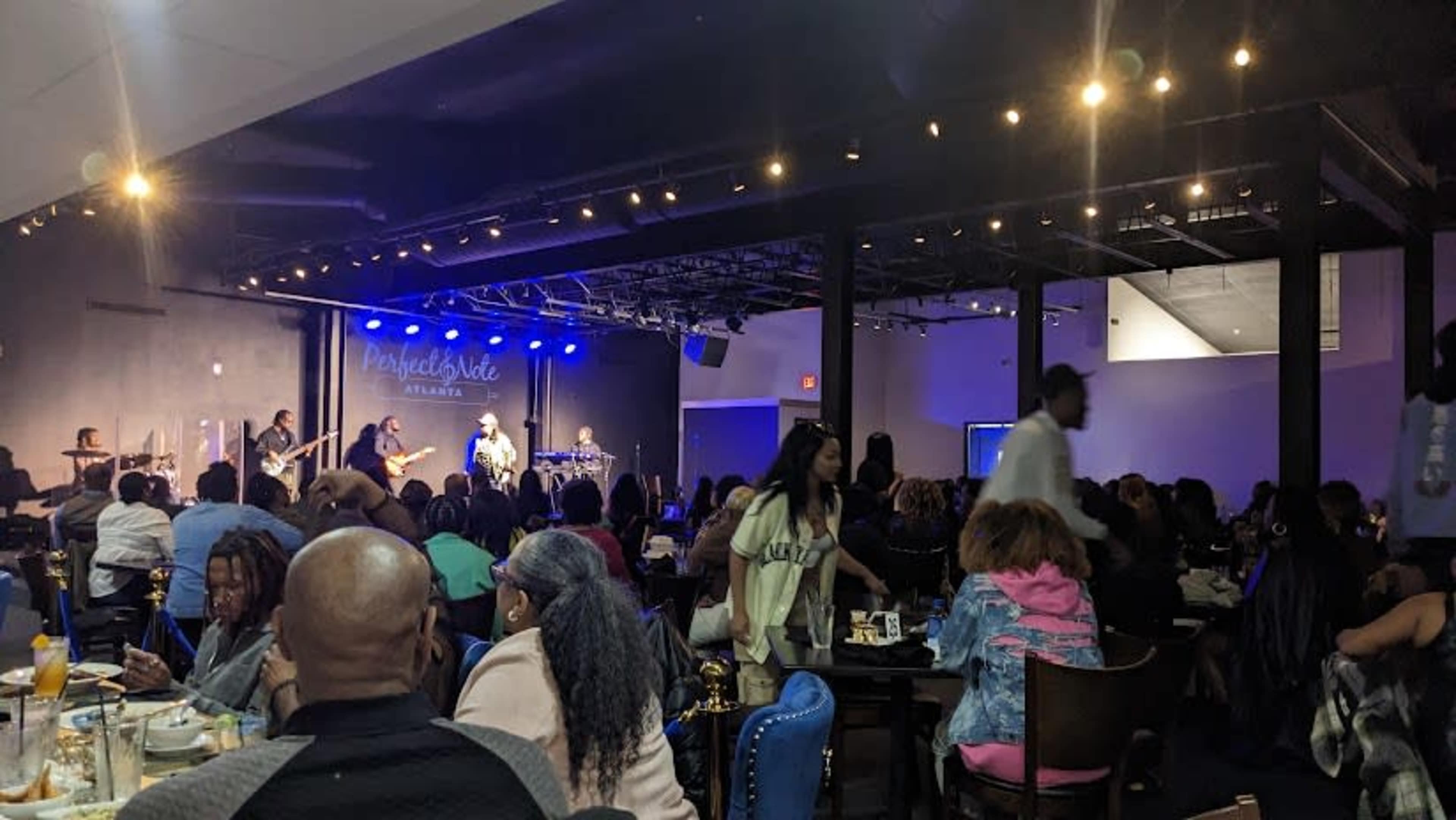 A lively venue features a band performing on stage as patrons enjoy their meals and socialize at tables.