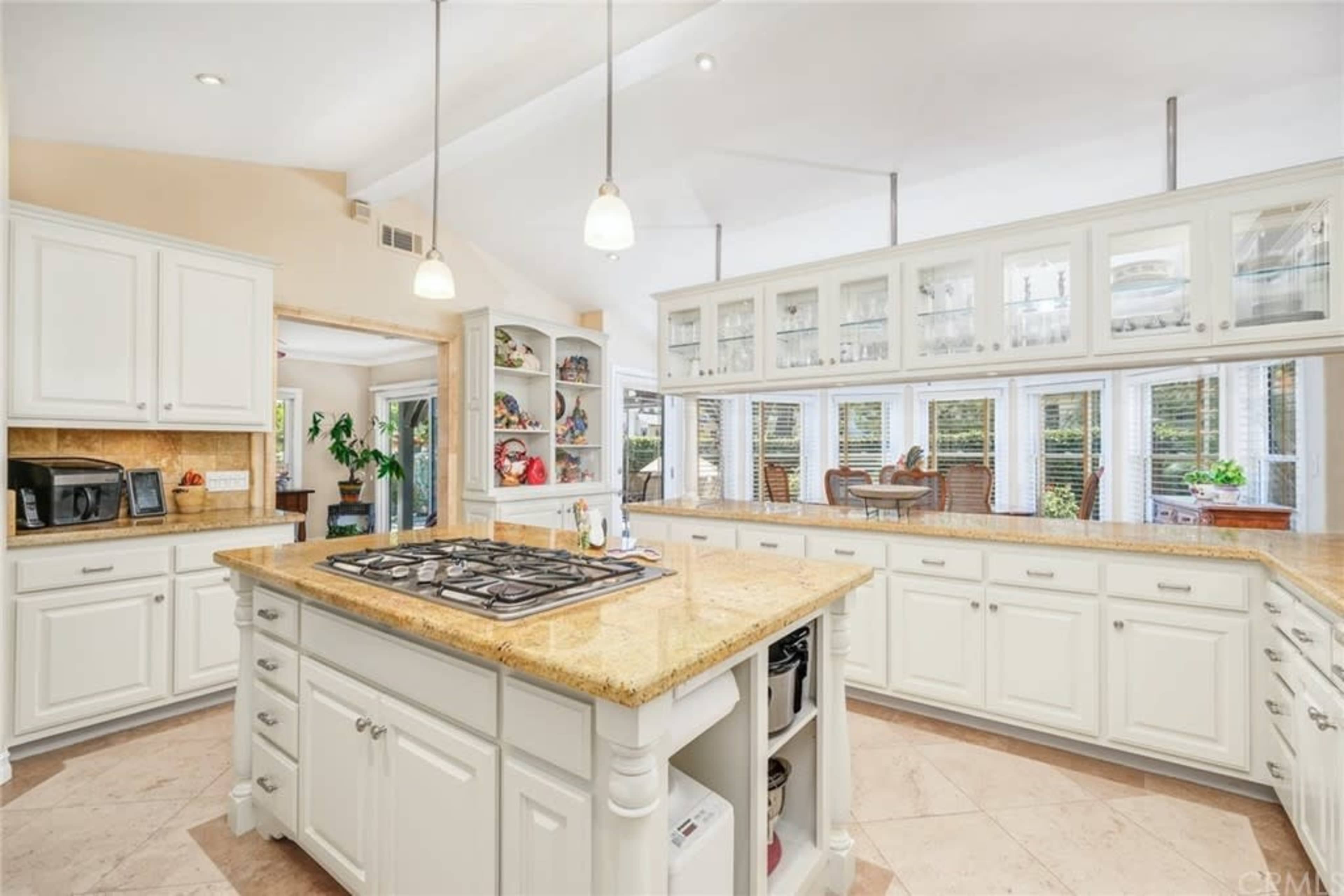 The kitchen features white cabinets, a central island with a gas cooktop, and large windows providing ample natural light.