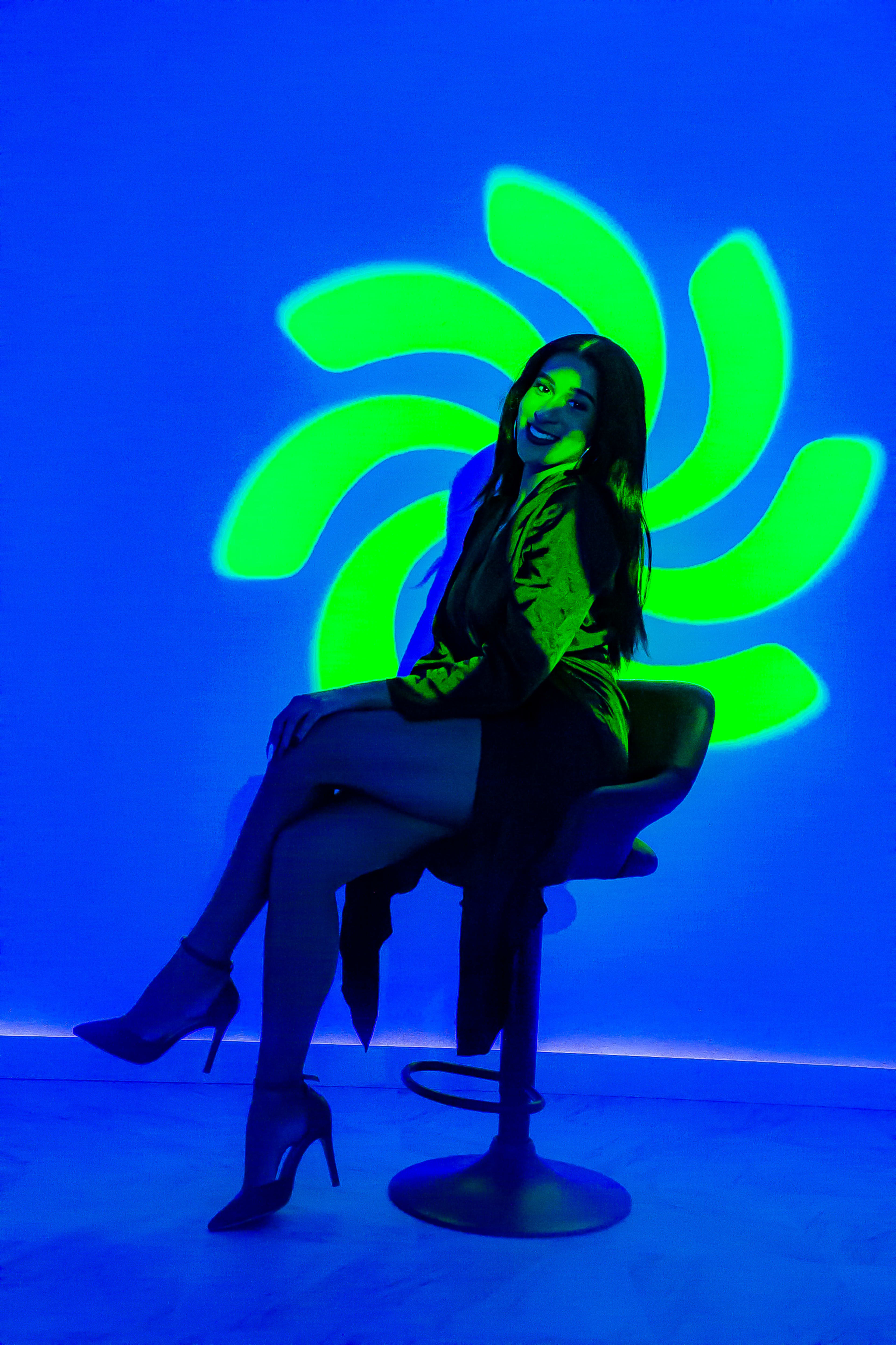 A fashion photoshoot of a woman on a chair in front of a neon blue wall.